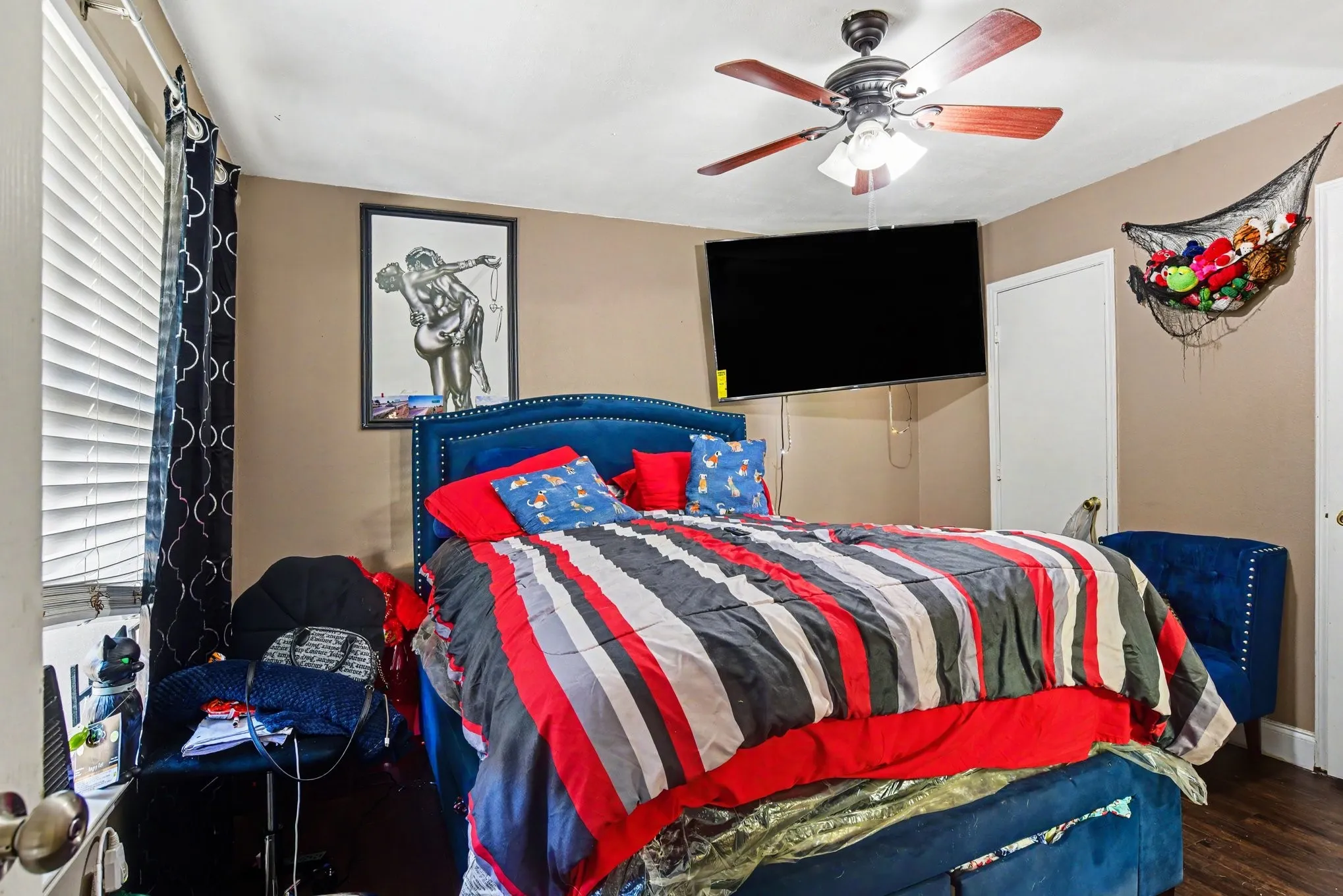 Primary bedroom suite featuring wall-mounted TV setup, central ceiling fan, and natural window lighting.