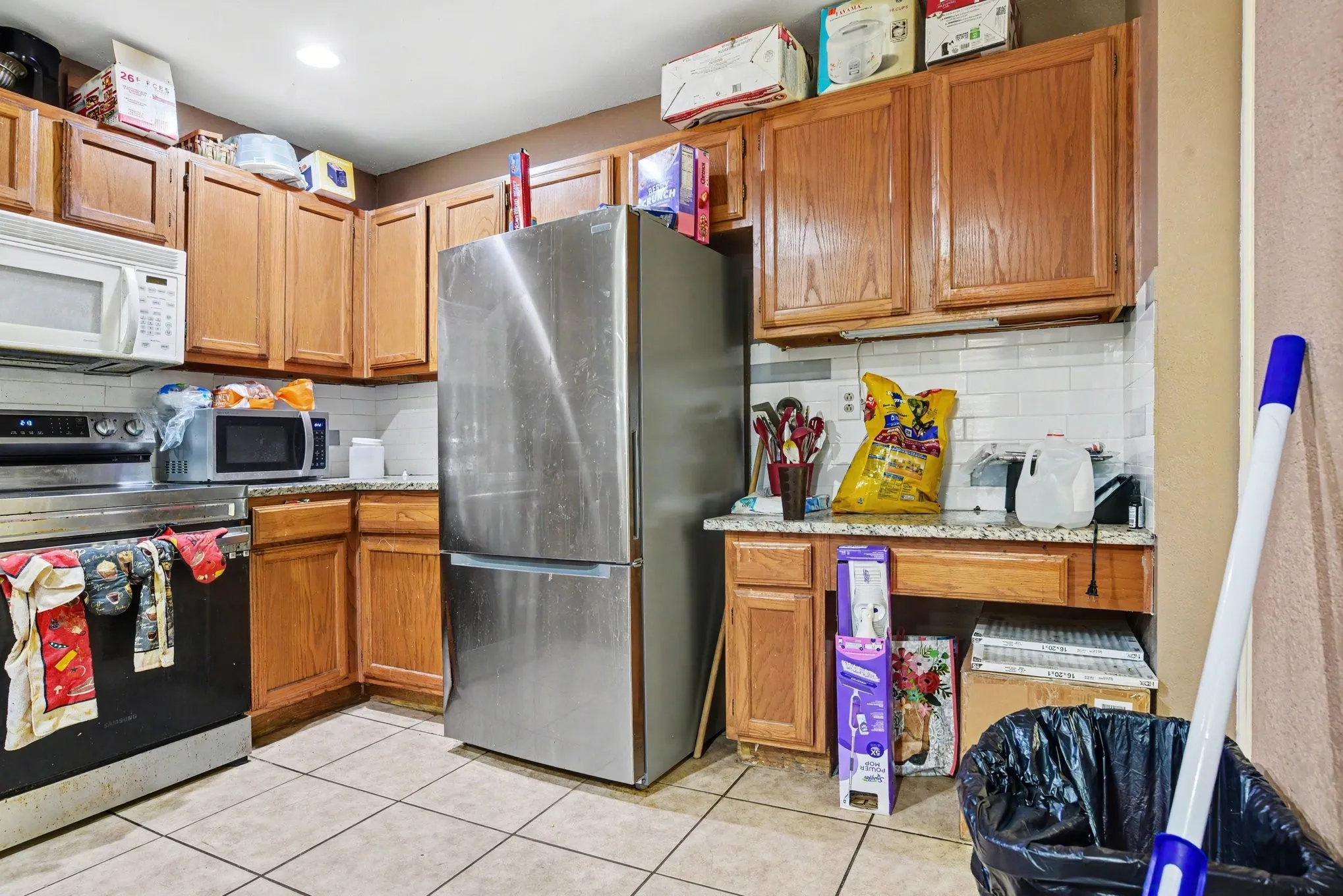 Functional kitchen equipped with warm wood cabinetry, stainless steel appliances, and durable tile flooring.