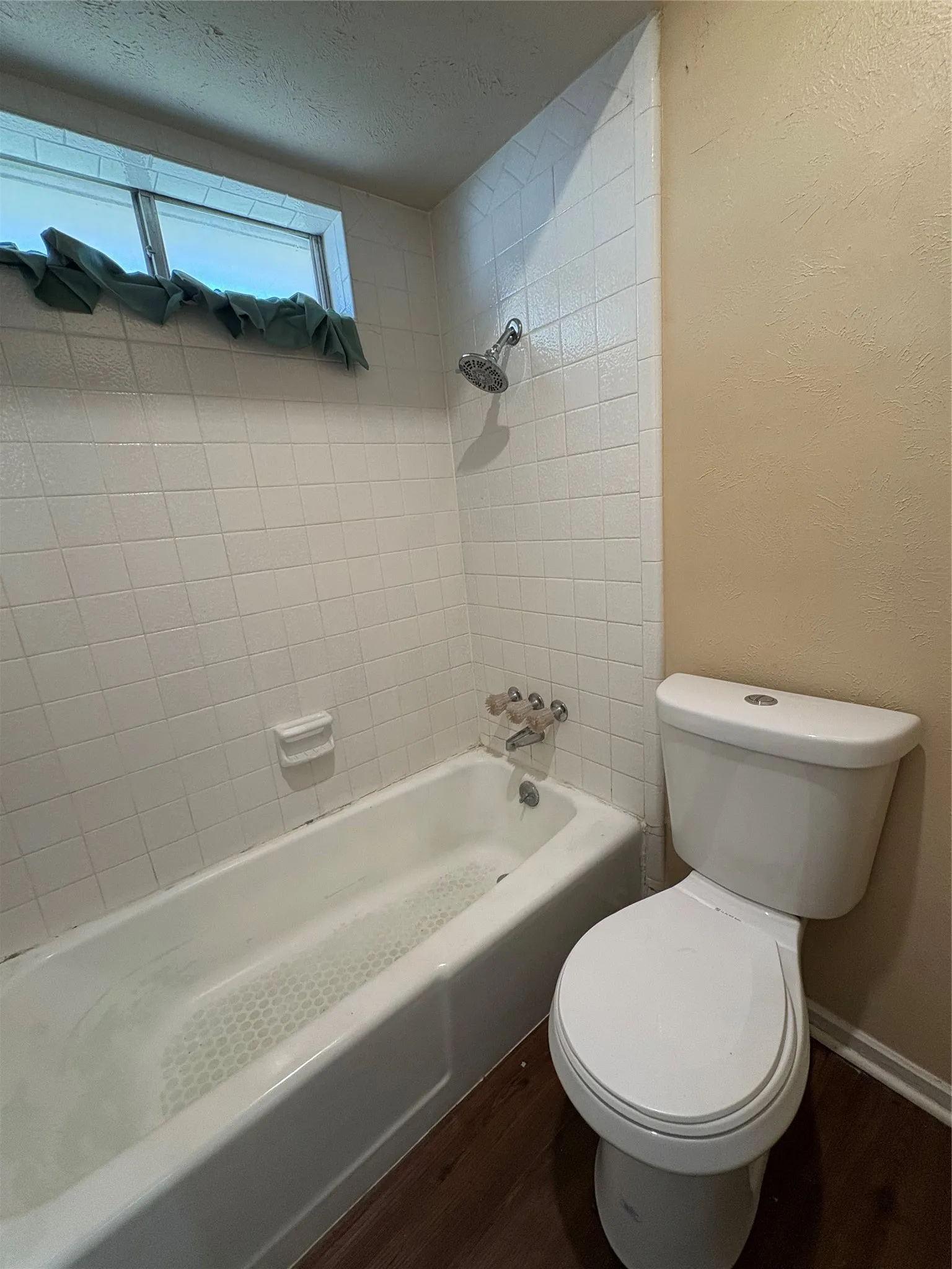 White tiled shower surround, bathtub, toilet, and wood-finish flooring