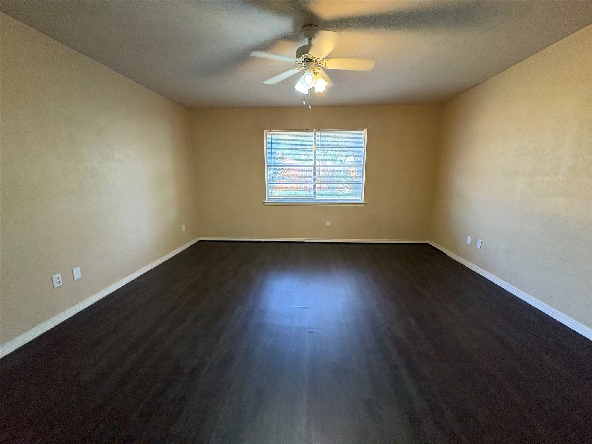 Spacious room featuring dark wood-finish flooring, a ceiling fan with integrated lighting, and a window with white trim