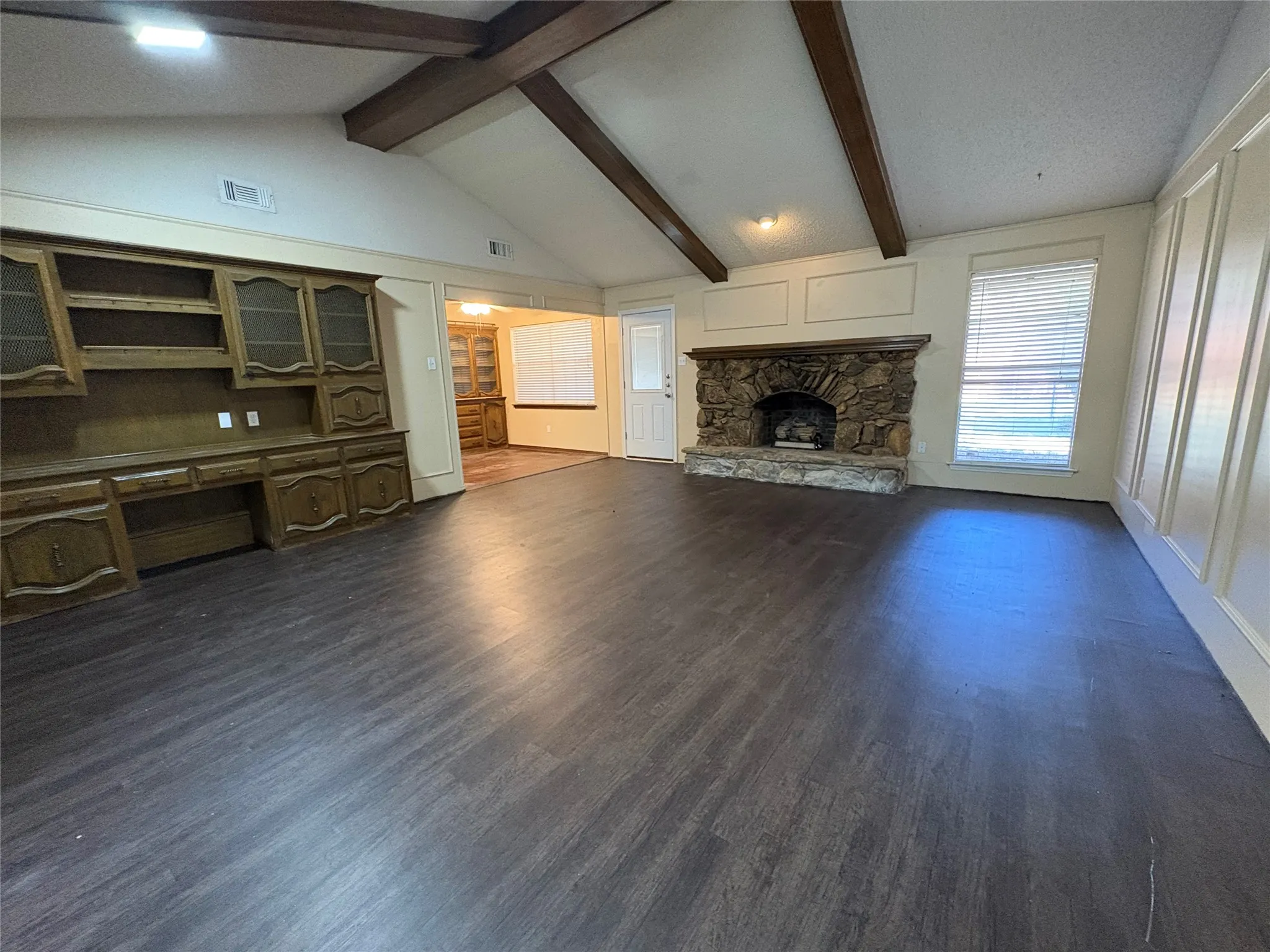 Vaulted ceiling with exposed wood beams, stone fireplace, wood-finish flooring, built-in cabinetry, and panel molding