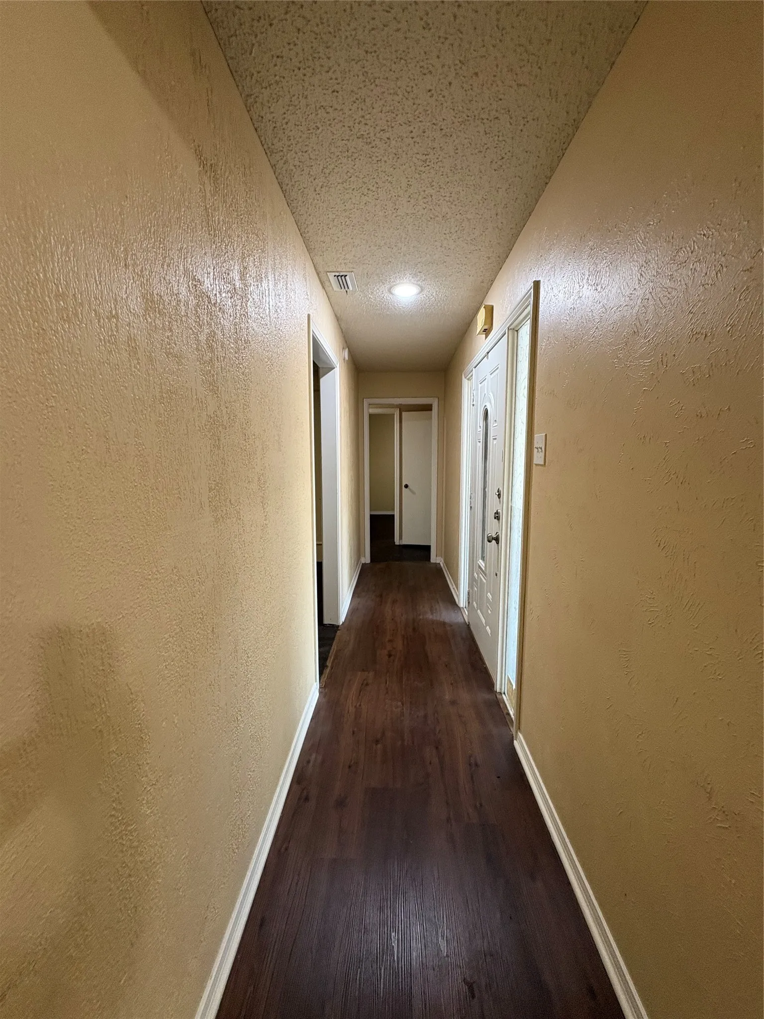 Long hallway featuring wood-finish flooring, recessed lighting, and a paneled entry door