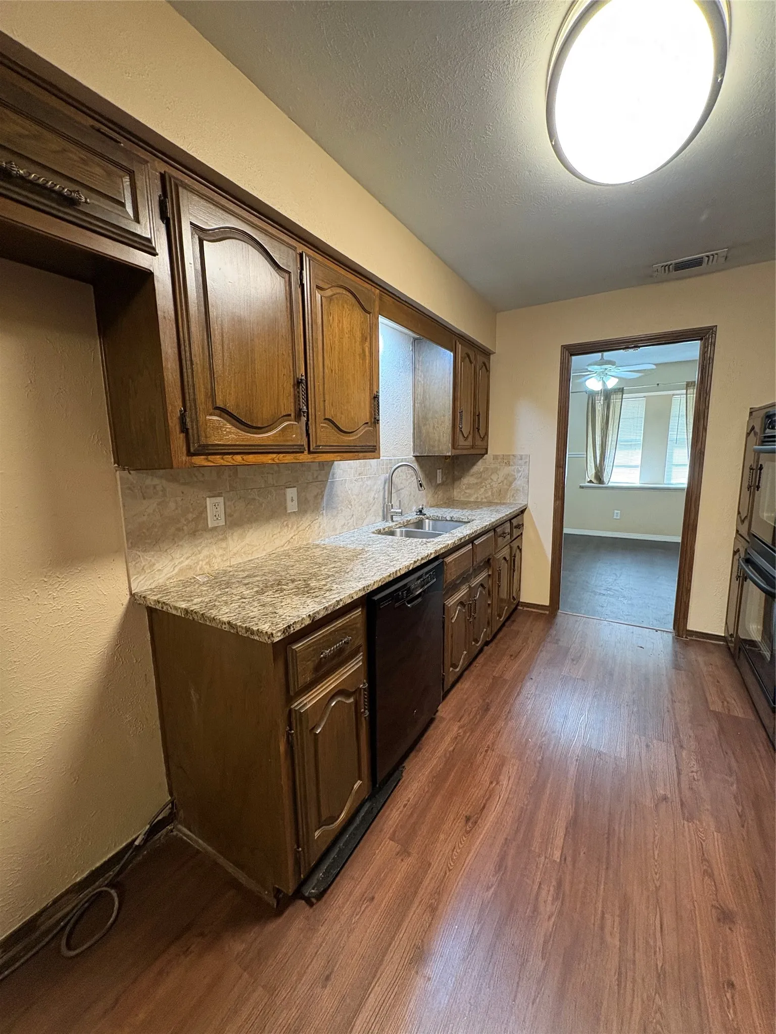 Kitchen featuring wood-finish flooring, wood cabinetry, stone-finish countertops, a stainless steel sink with a gooseneck faucet, and a built-in dishwasher