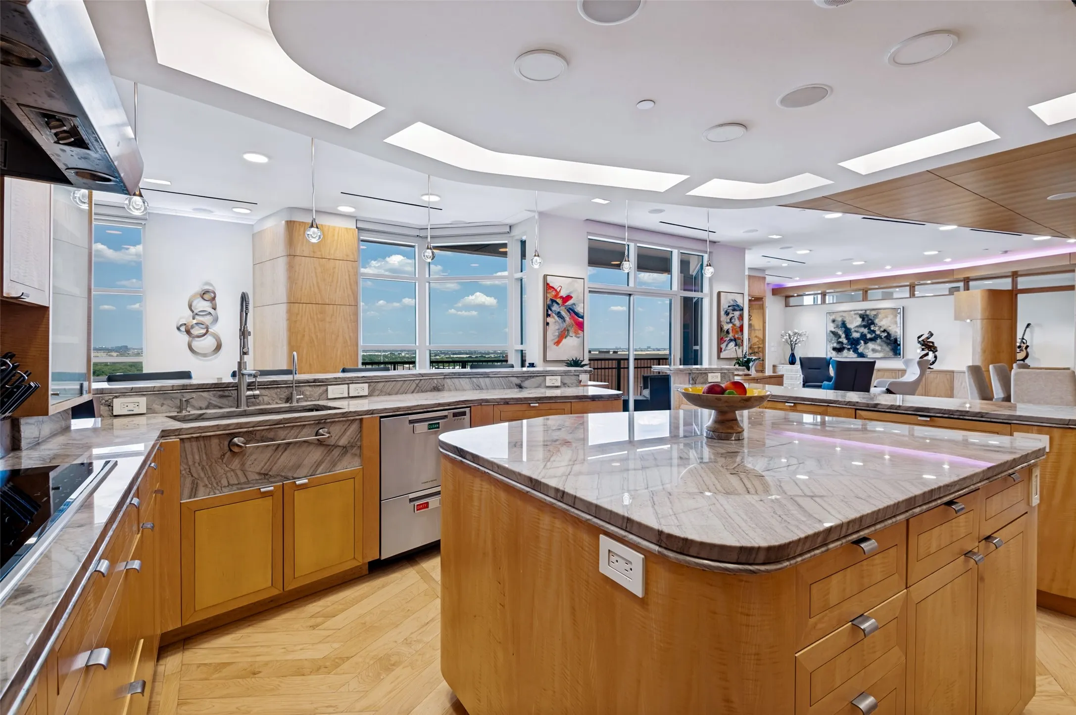 Gourmet kitchen featuring dual islands with waterfall-edge countertops, warm wood-finish cabinetry, stainless steel appliances, and expansive windows overlooking landscaped grounds