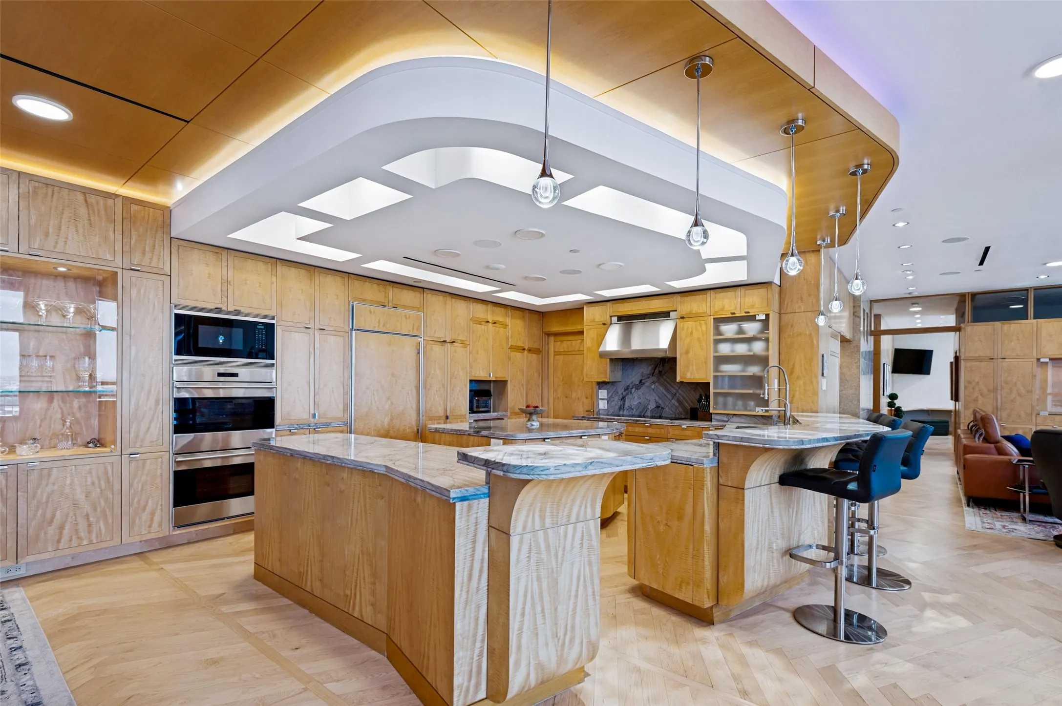 Gourmet kitchen featuring custom wood cabinetry, stainless steel dual wall ovens, quartz countertops, a large center island with seating, pendant lighting, and an architectural coffered ceiling with integrated skylights