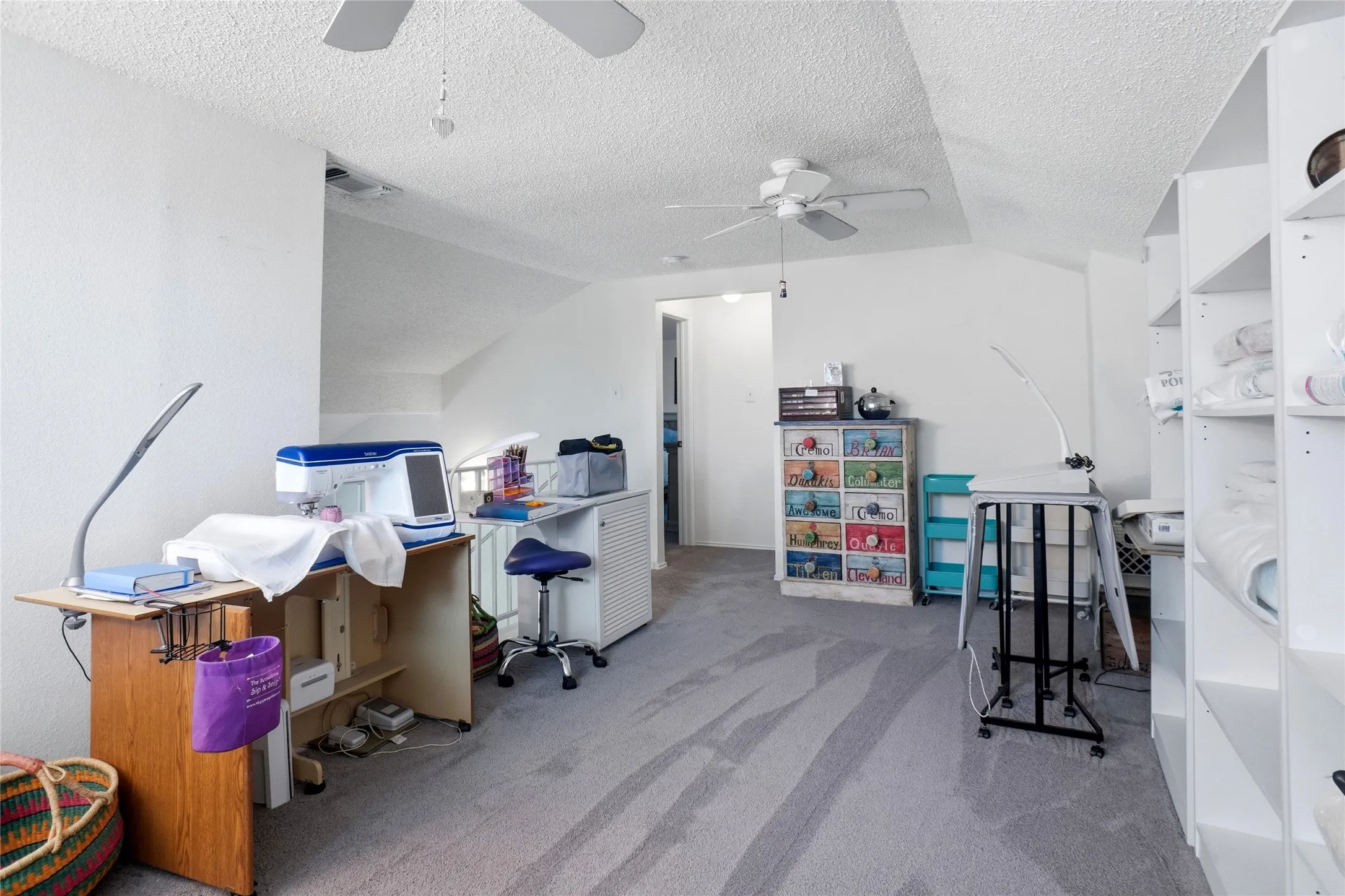 Vaulted ceilings with textured finish, light grey carpeting, recessed wall area, ceiling fan with light fixture, and white built-in shelving