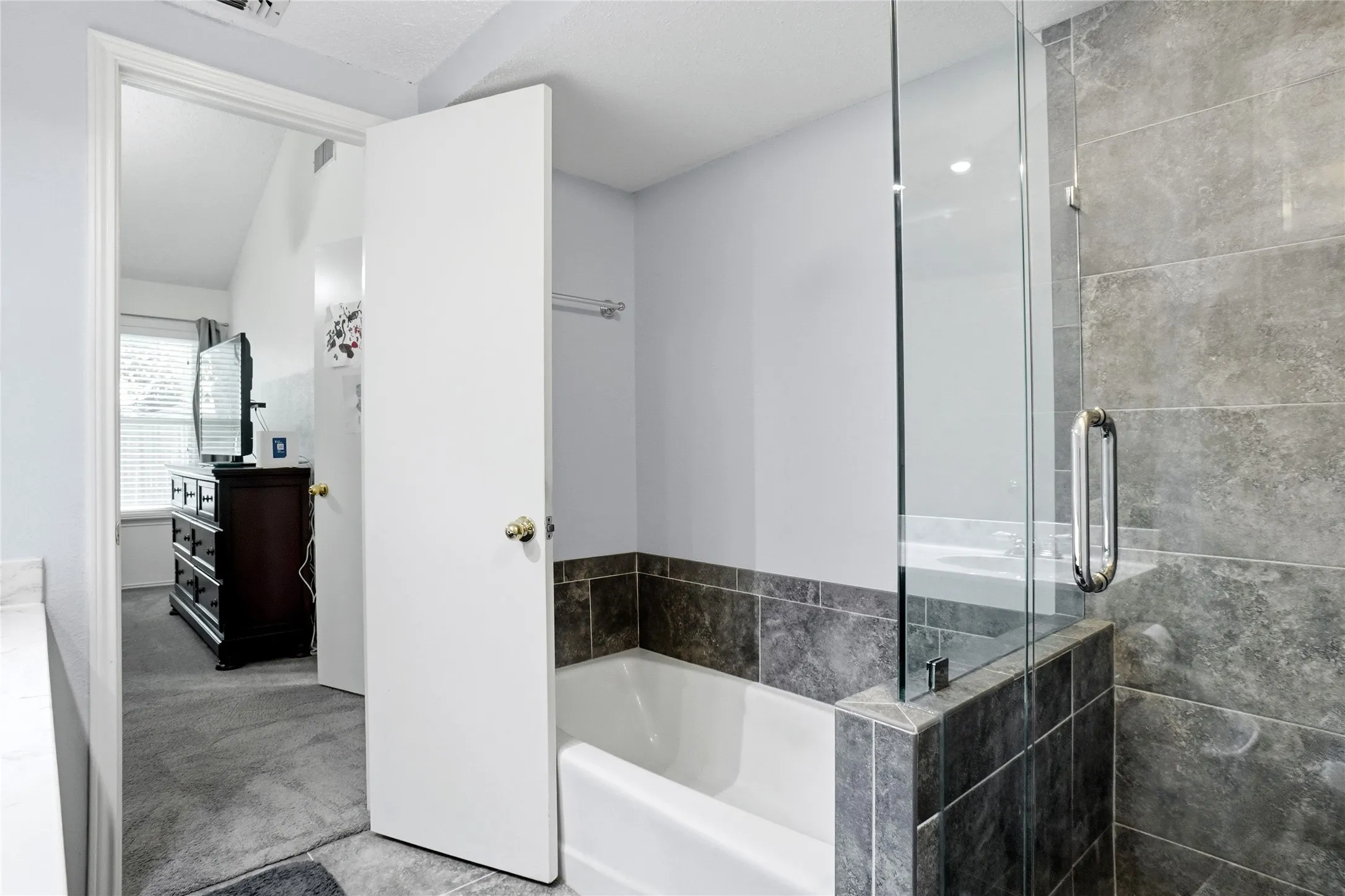 Bathtub with dark gray tile surround and glass shower enclosure
