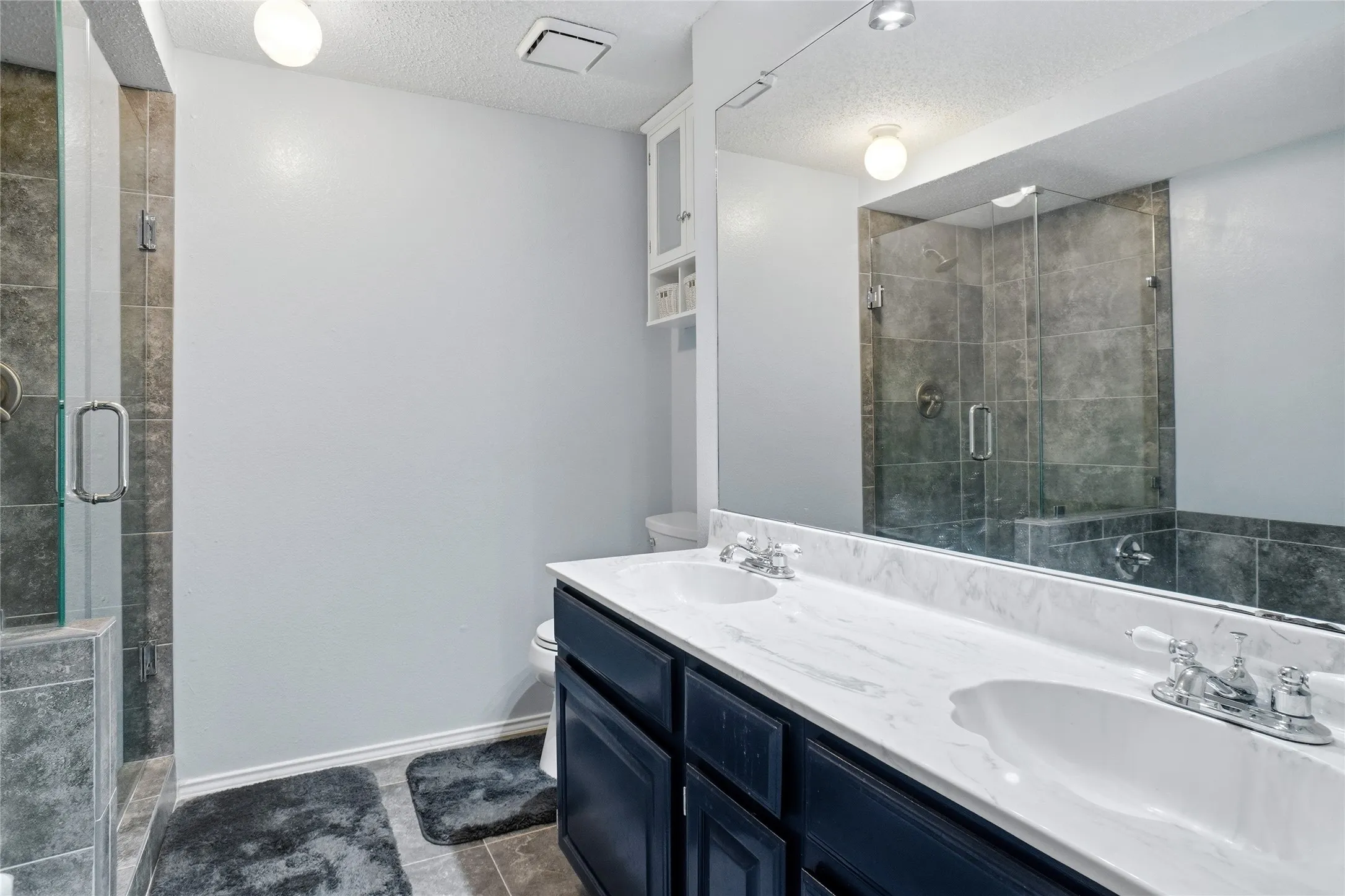 Dual vanity with undermount sinks, white countertop, dark wood-finish cabinetry, and a walk-in shower with tile surround and glass enclosure