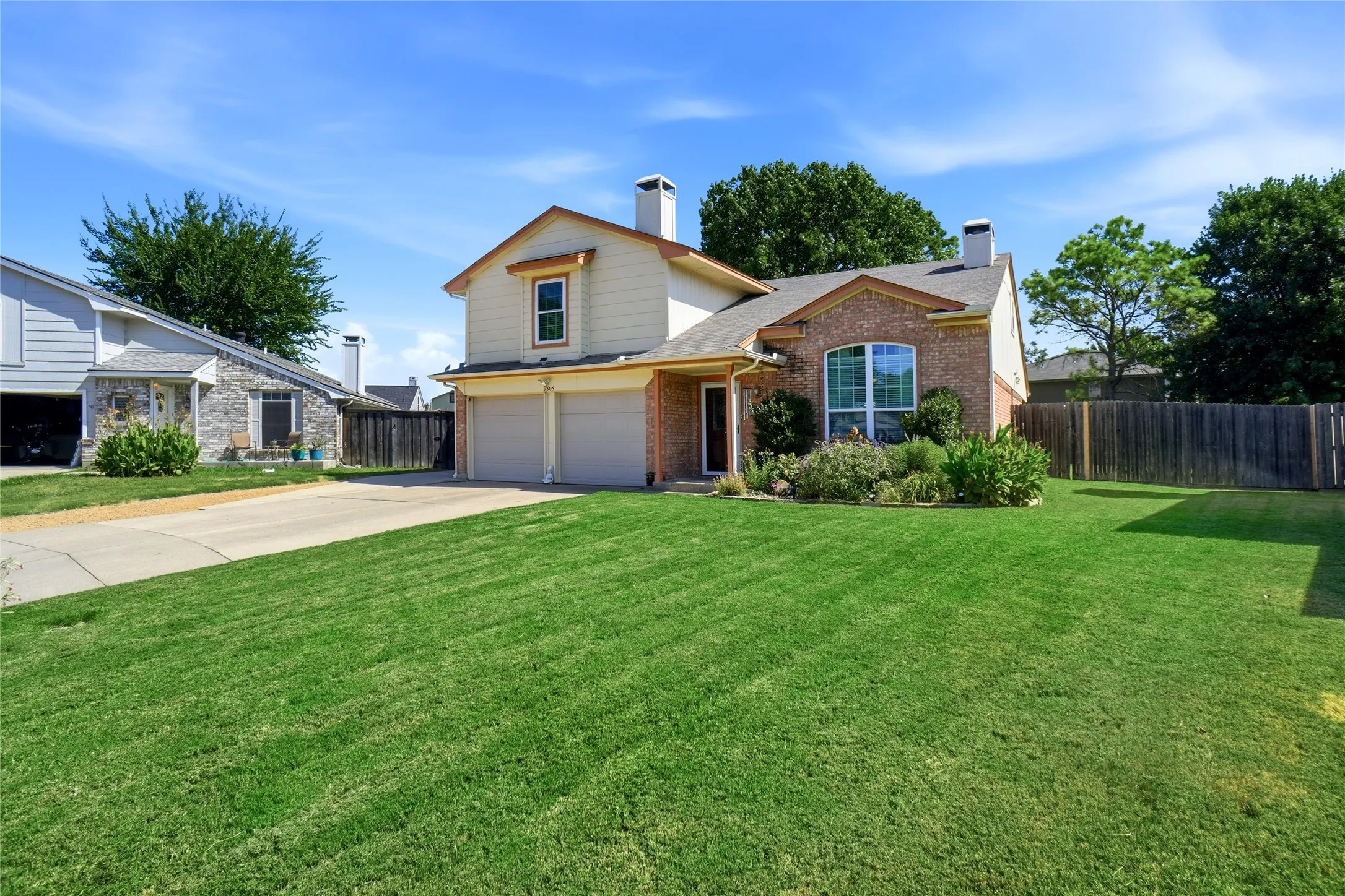 Two-story exterior with brick and siding facade, two-car garage, front landscaping, and a fenced backyard