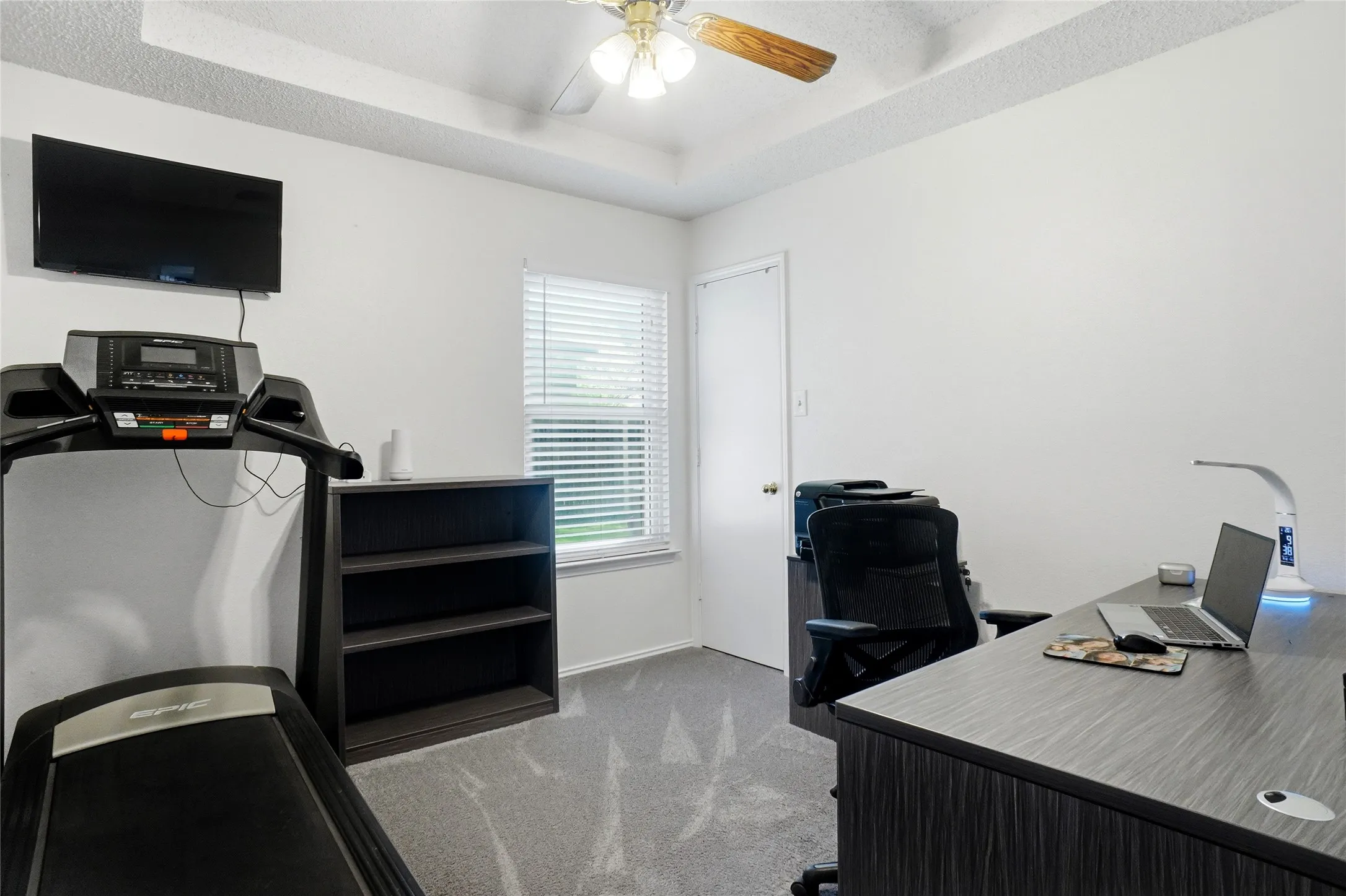Tray ceiling with a ceiling fan, light gray carpet, and a window with blinds