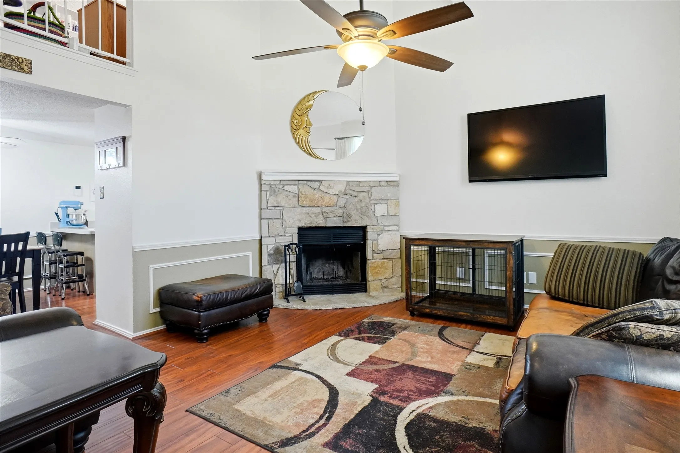 Stone-surround fireplace with a black firebox, wood-finish flooring, and a ceiling fan with integrated lighting