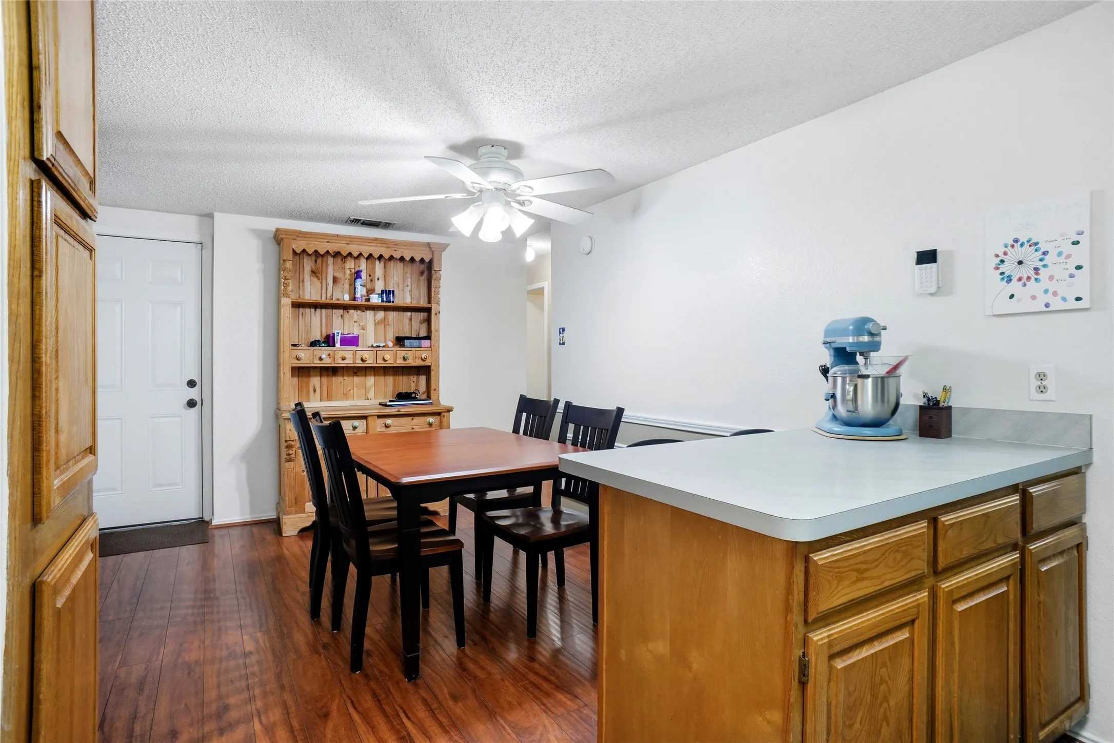 Wood-finish flooring, white ceiling fan, white paneled door, and built-in wood cabinetry with a light countertop