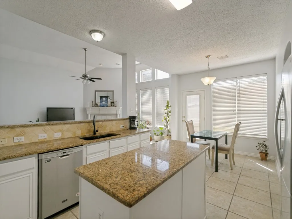 Kitchen featuring a center island with a granite-style countertop, white cabinetry, integrated stainless steel dishwasher, and tile flooring