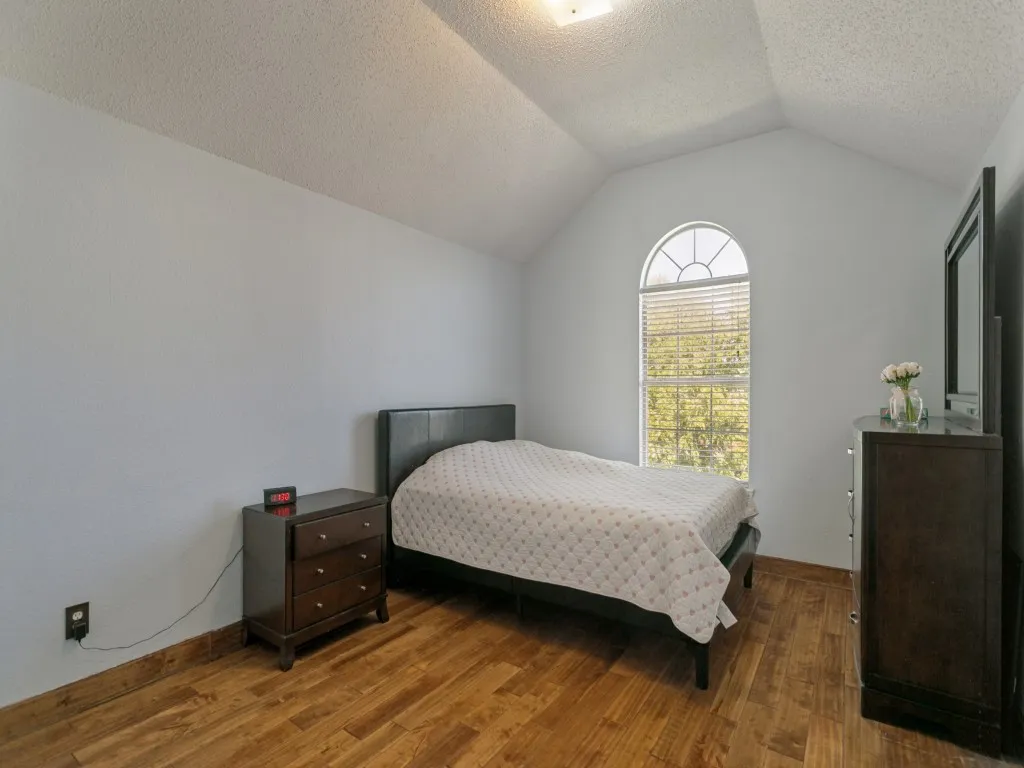 Vaulted ceiling with an arched window featuring blinds, complemented by wood-finish flooring