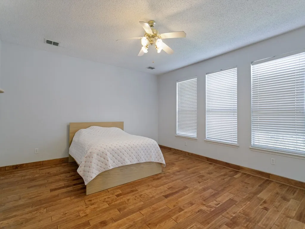 Recessed ceiling light, ceiling fan with light kit, three windows with blinds, wood-finish flooring, and white painted walls