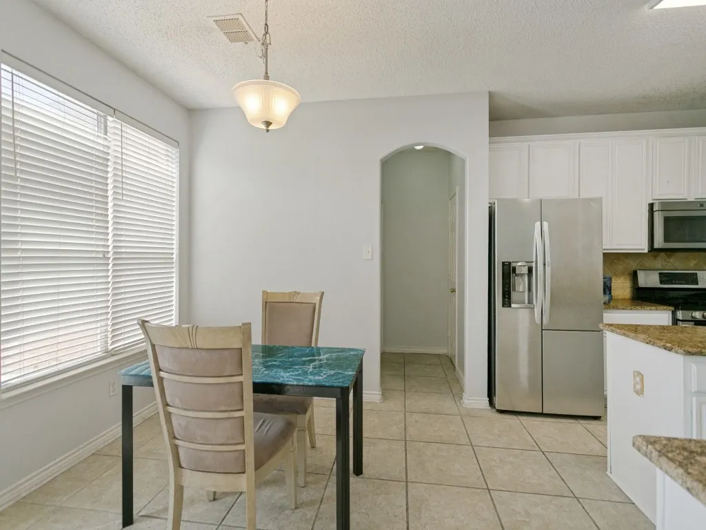 Kitchen area with tile flooring, white cabinetry, stainless steel refrigerator, and a kitchen island with a stone-finish countertop