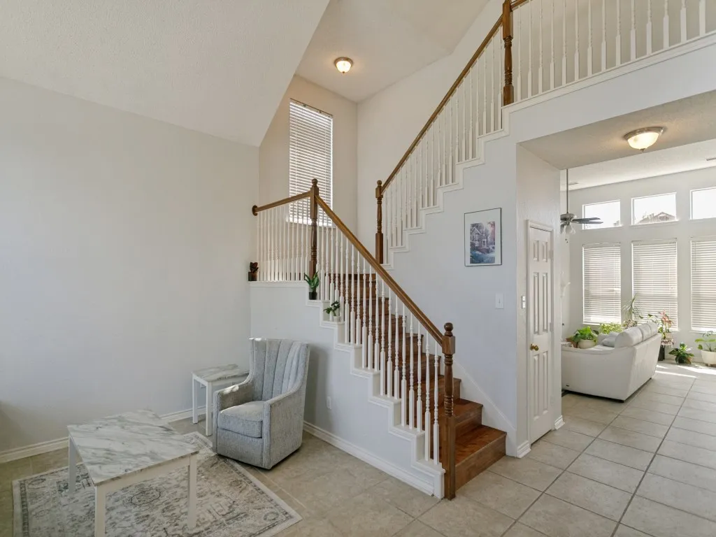 Two-story entry featuring a wood-finish staircase with white balusters, ceramic tile flooring, and a window with blinds