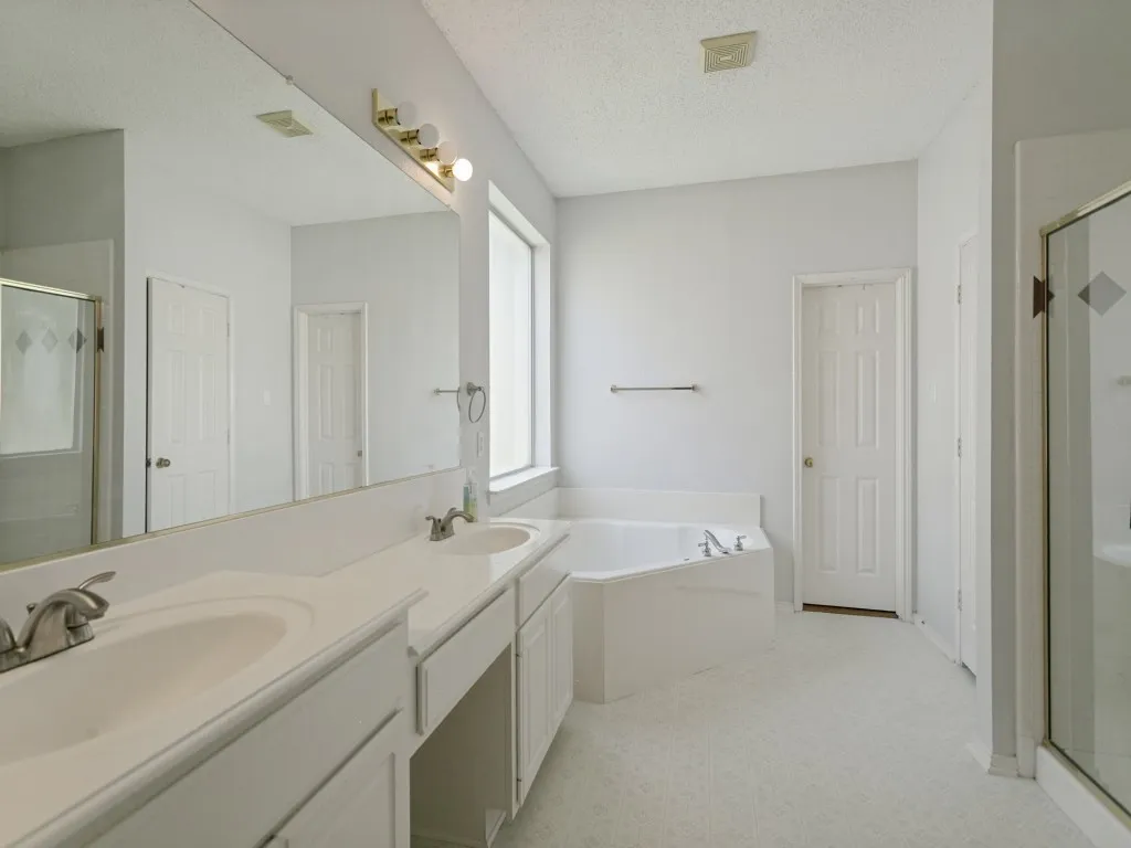 Dual vanity with integrated sinks, corner soaking tub, and a glass-enclosed shower
