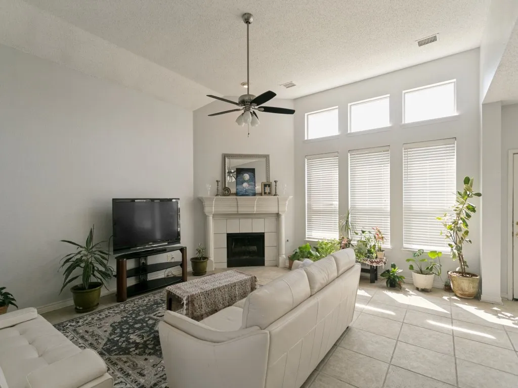 Vaulted ceiling with a ceiling fan, fireplace with a decorative mantel, multiple windows with blinds, and tile flooring