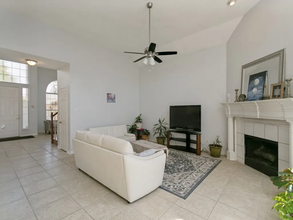 Spacious living area featuring a vaulted ceiling with a ceiling fan, a fireplace with a decorative mantel and tile surround, and light-toned tile flooring