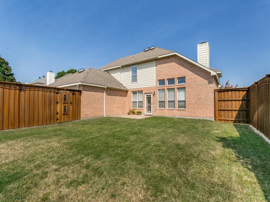 Expansive backyard featuring a manicured lawn, brick exterior, and a private wooden fence with an arched gate