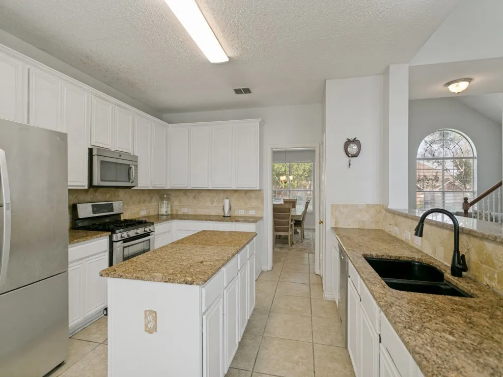 White cabinetry, stainless steel appliances, granite countertops, tile flooring, and a kitchen island