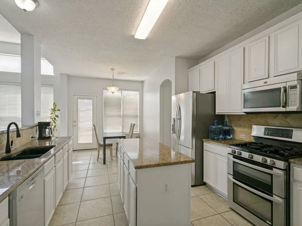 White cabinetry, stainless steel appliances, dual ovens, granite countertops, and tiled flooring