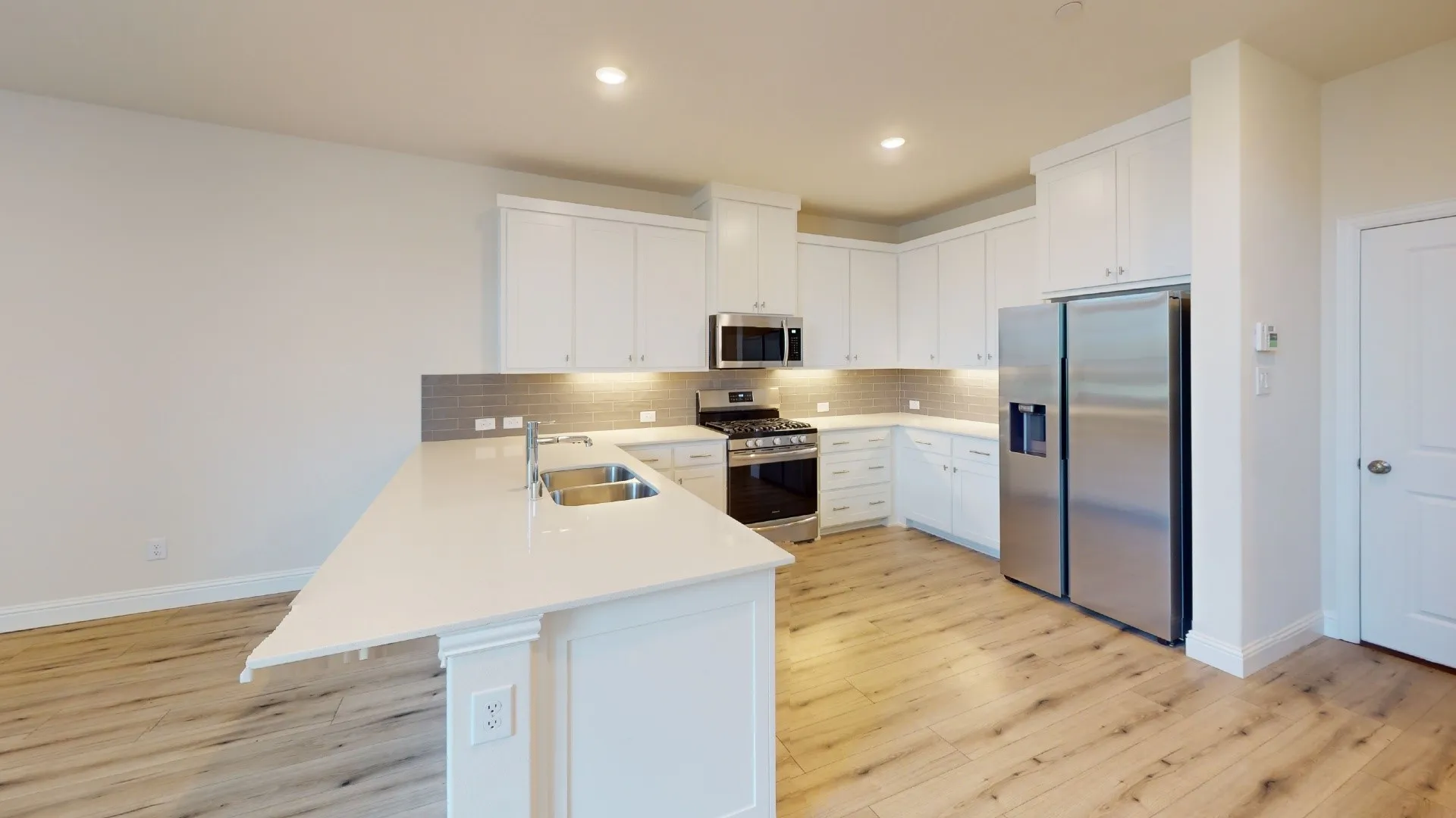 Kitchen featuring wood-finish flooring, white cabinetry, stainless steel appliances, and an island with a dual basin sink
