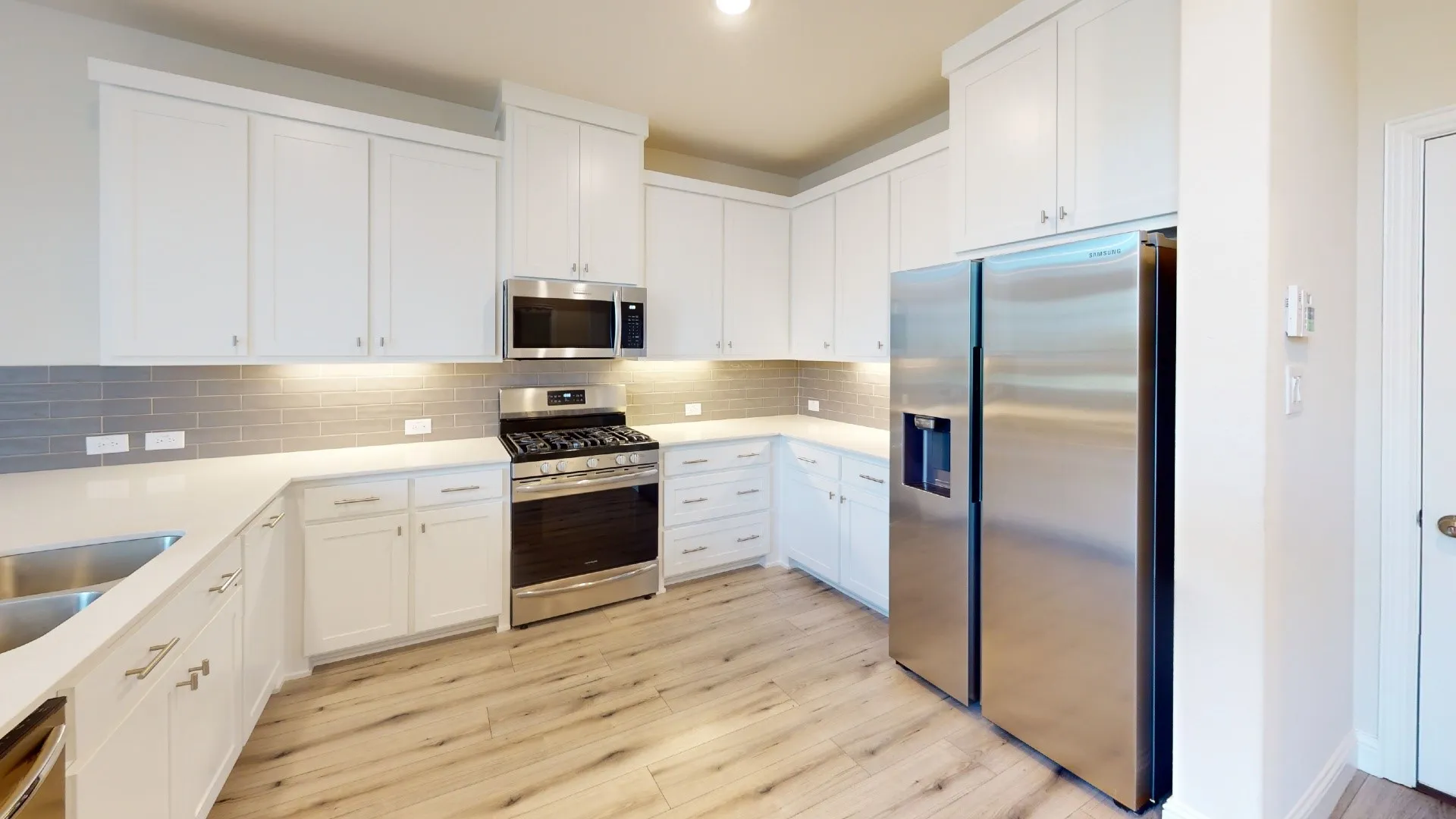 Kitchen featuring white shaker cabinetry, stainless steel appliances, light-toned countertops, subway tile backsplash, and wood-finish flooring