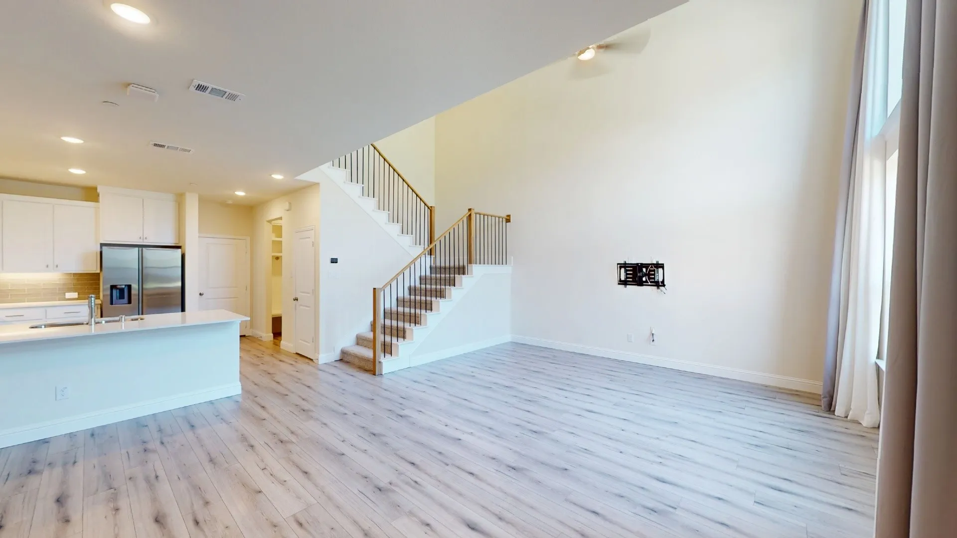 Open concept living area with wood-finish flooring, vaulted ceiling, and a prominent staircase with wood railings
