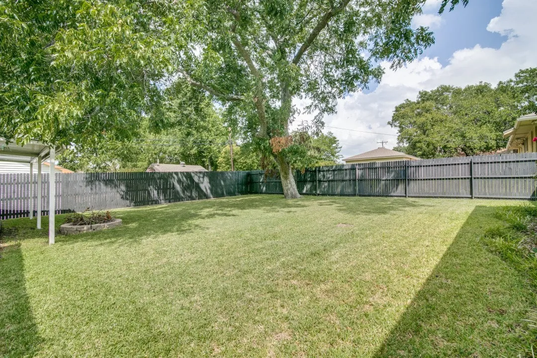 Expansive backyard featuring a manicured lawn, established shade tree, and wood privacy fencing
