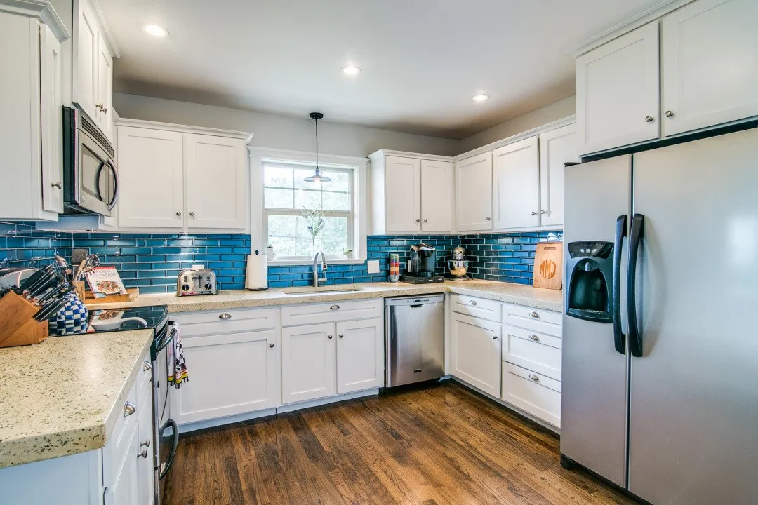 White cabinetry, stainless steel appliances, vibrant blue subway tile backsplash, light speckled countertops, and wood-finish flooring