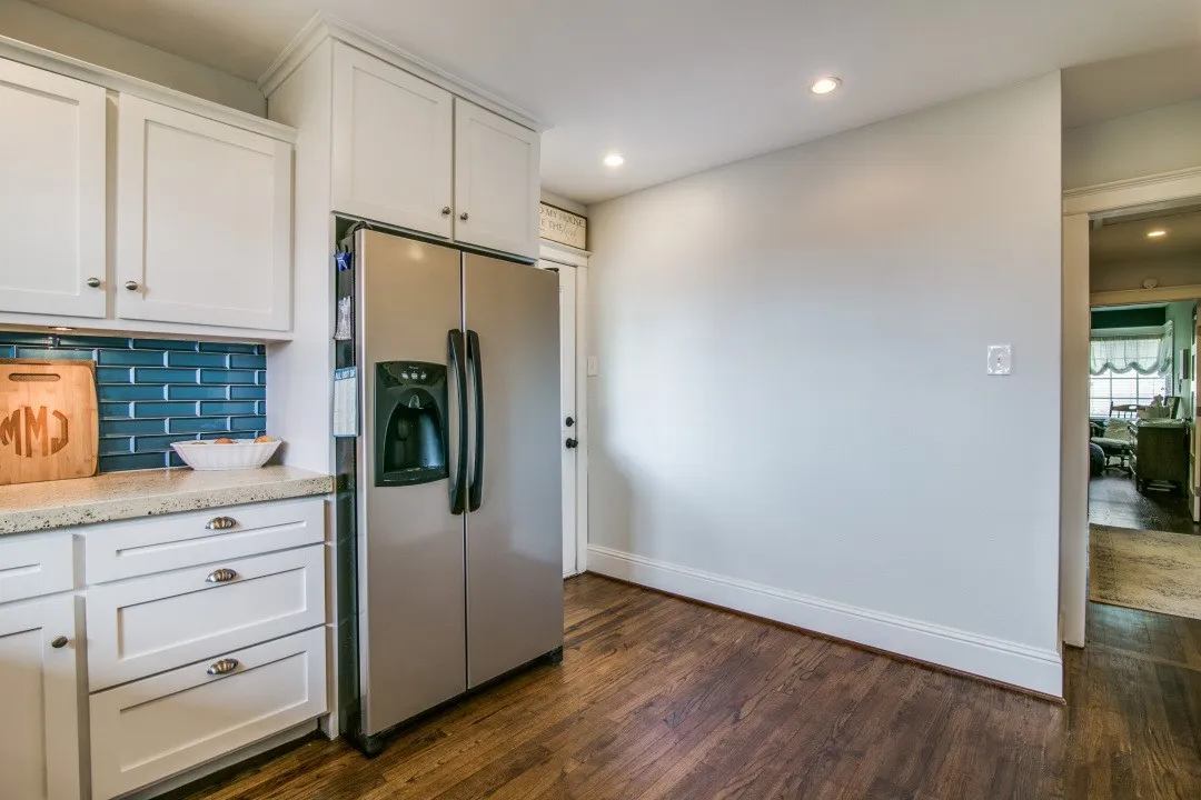 White cabinetry with crown molding, stainless steel refrigerator, white countertops, and wood-finish flooring