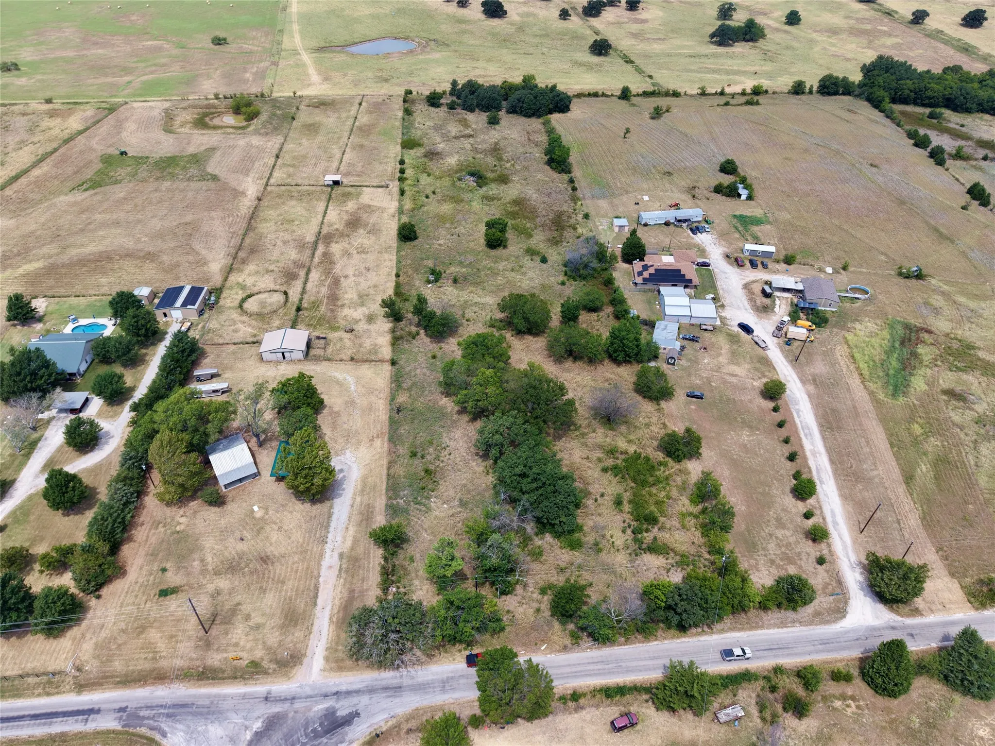 Expansive property featuring multiple structures, a swimming pool, and mature trees, bordered by a paved road