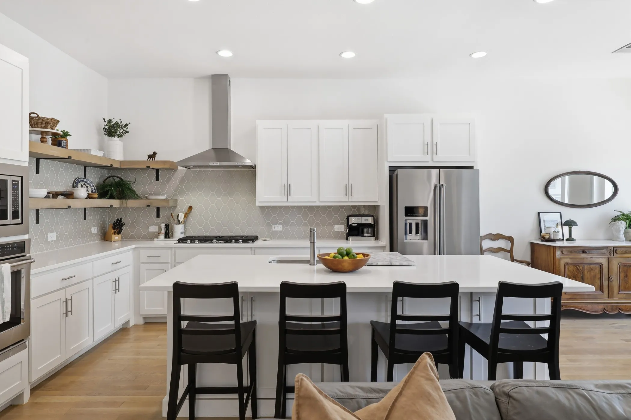 Contemporary kitchen featuring a large island with seating, stainless steel appliances, open shelving, white cabinetry, and wood-finish flooring