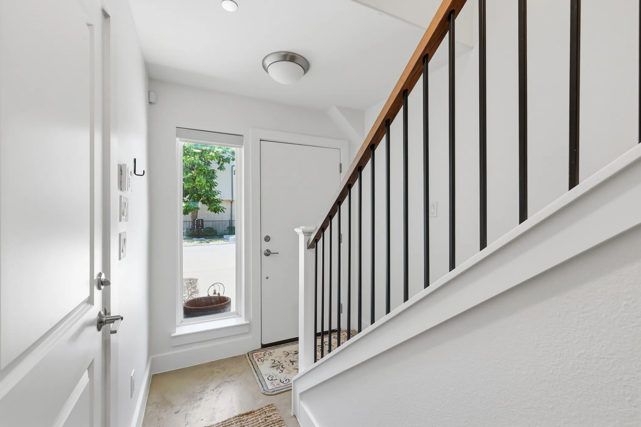 Entryway featuring a wood-finish handrail with black metal balusters, a built-in recessed light, and a fixed window