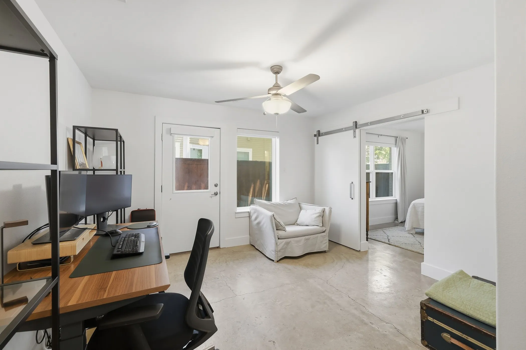 White interior paint, ceiling fan with light fixture, exterior door with window, window with trim, and a barn door on a metal track