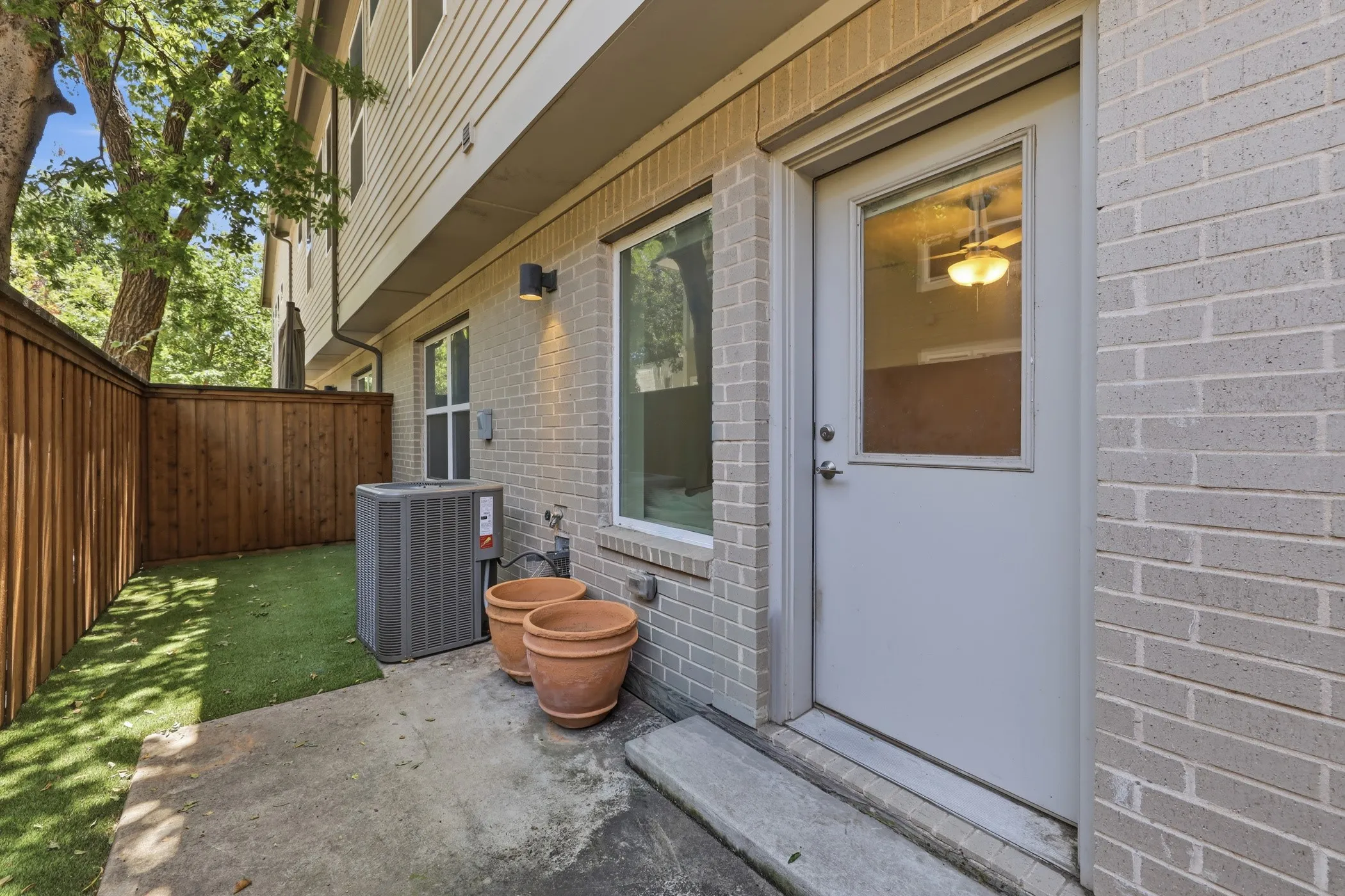Patio area featuring light-toned brick exterior, wood privacy fencing, and an exterior door with integrated window panel