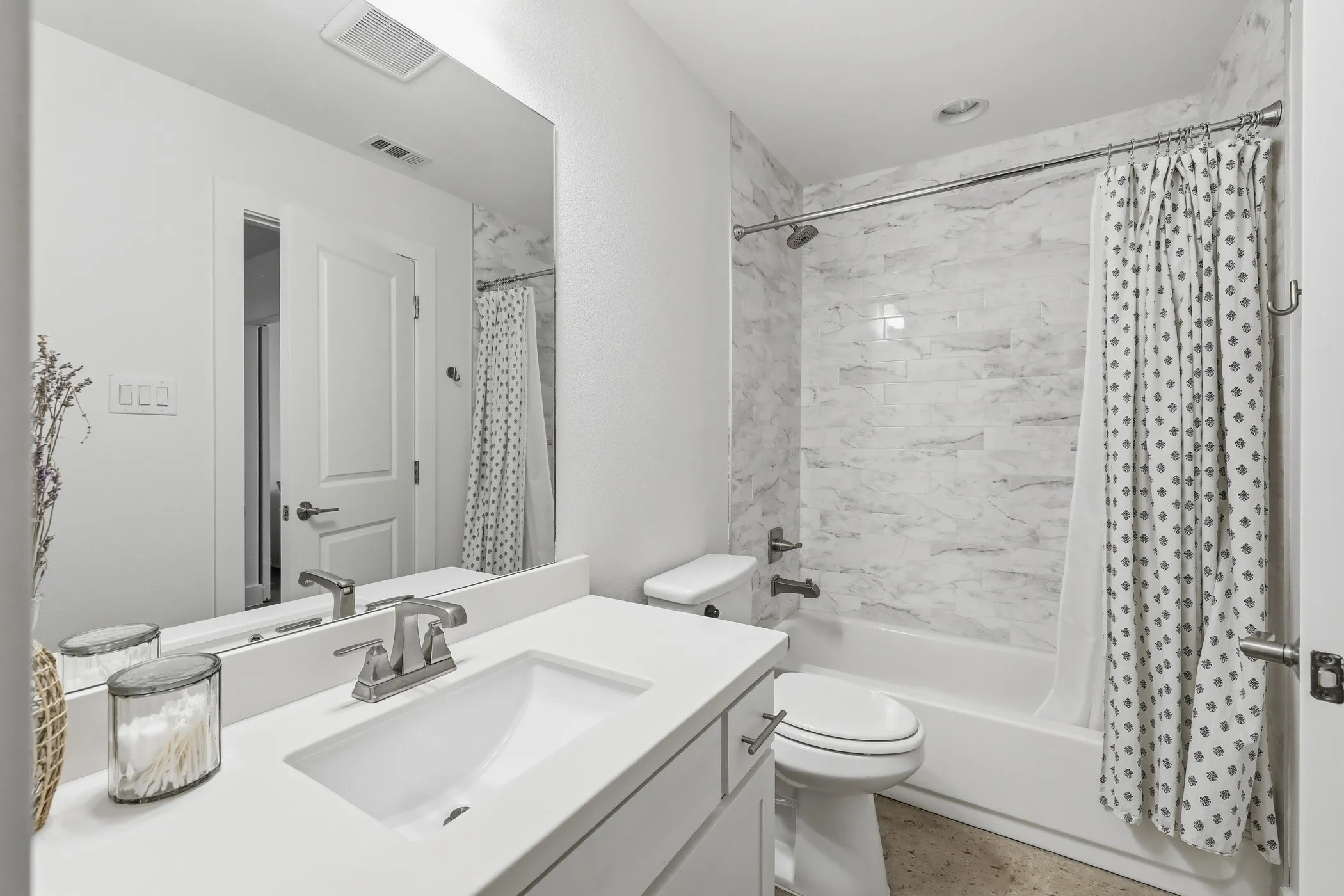 Bathroom featuring a white vanity with an integrated sink, brushed nickel faucet, a large wall mirror, and a full-size tub with a tile surround