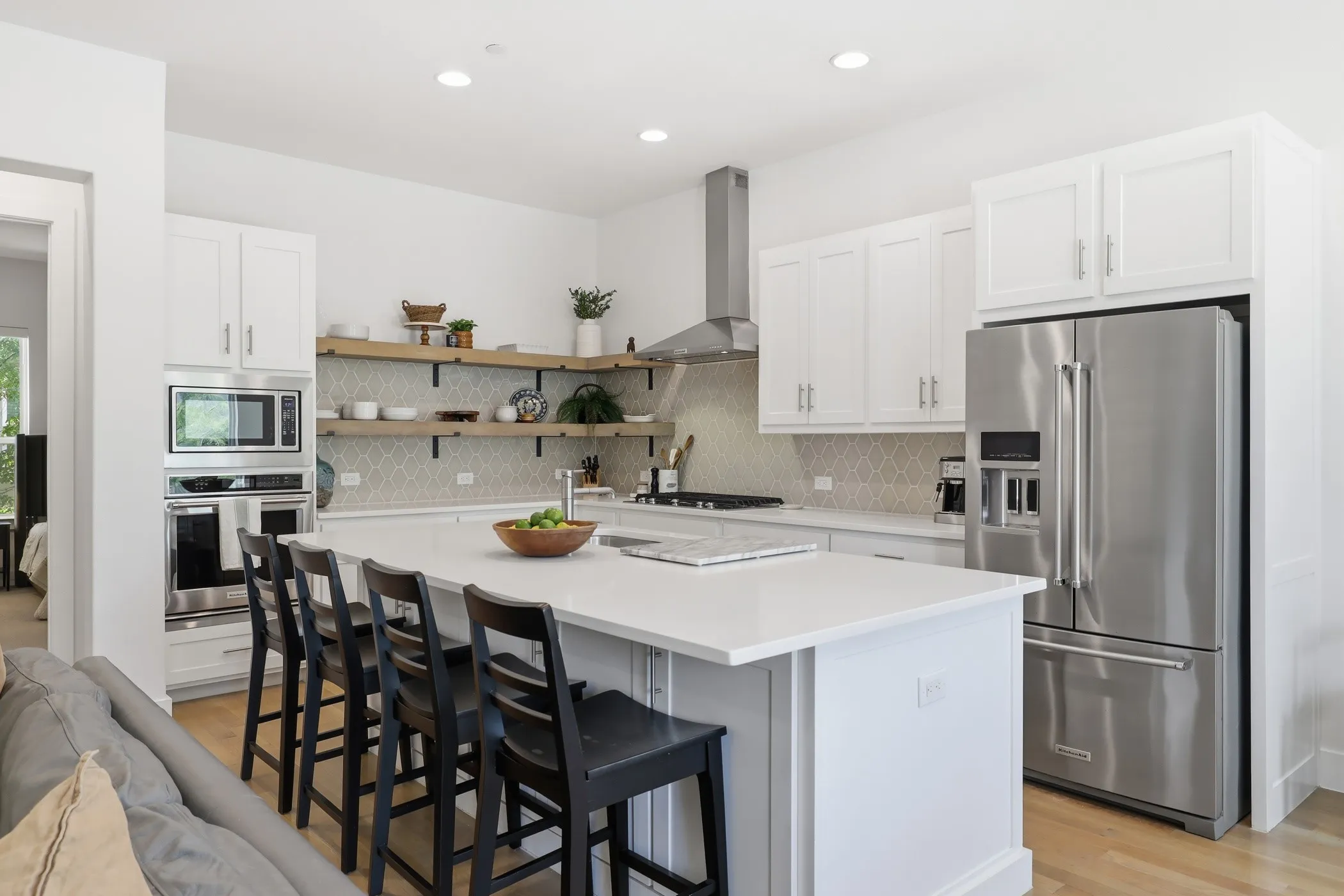 Kitchen featuring a large island with seating, white shaker cabinetry, stainless steel appliances, and wood-finish flooring