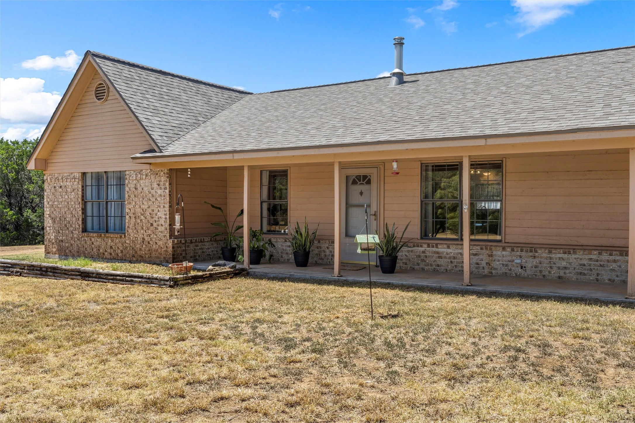 Front exterior featuring brick and siding, a covered porch, multiple windows, and a shingled roof