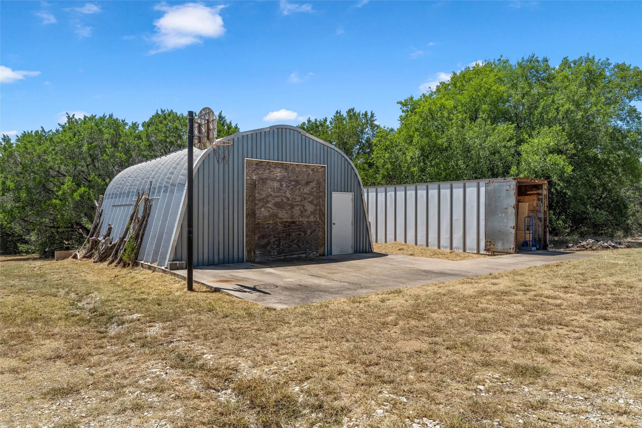 Metal quonset hut with a boarded main entry, side door, and concrete pad