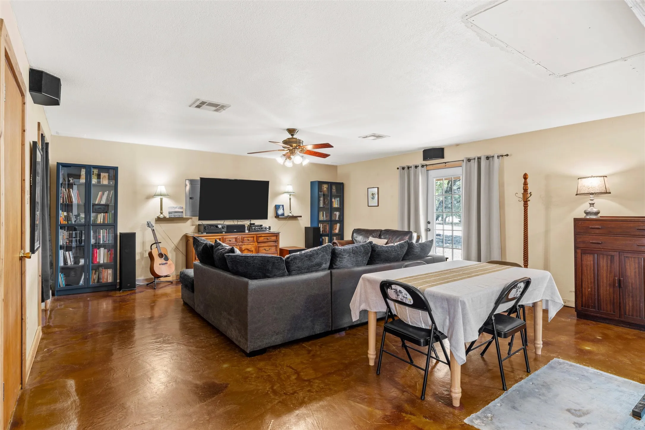 Expansive living area with high ceilings, durable concrete flooring, and a ceiling fan
