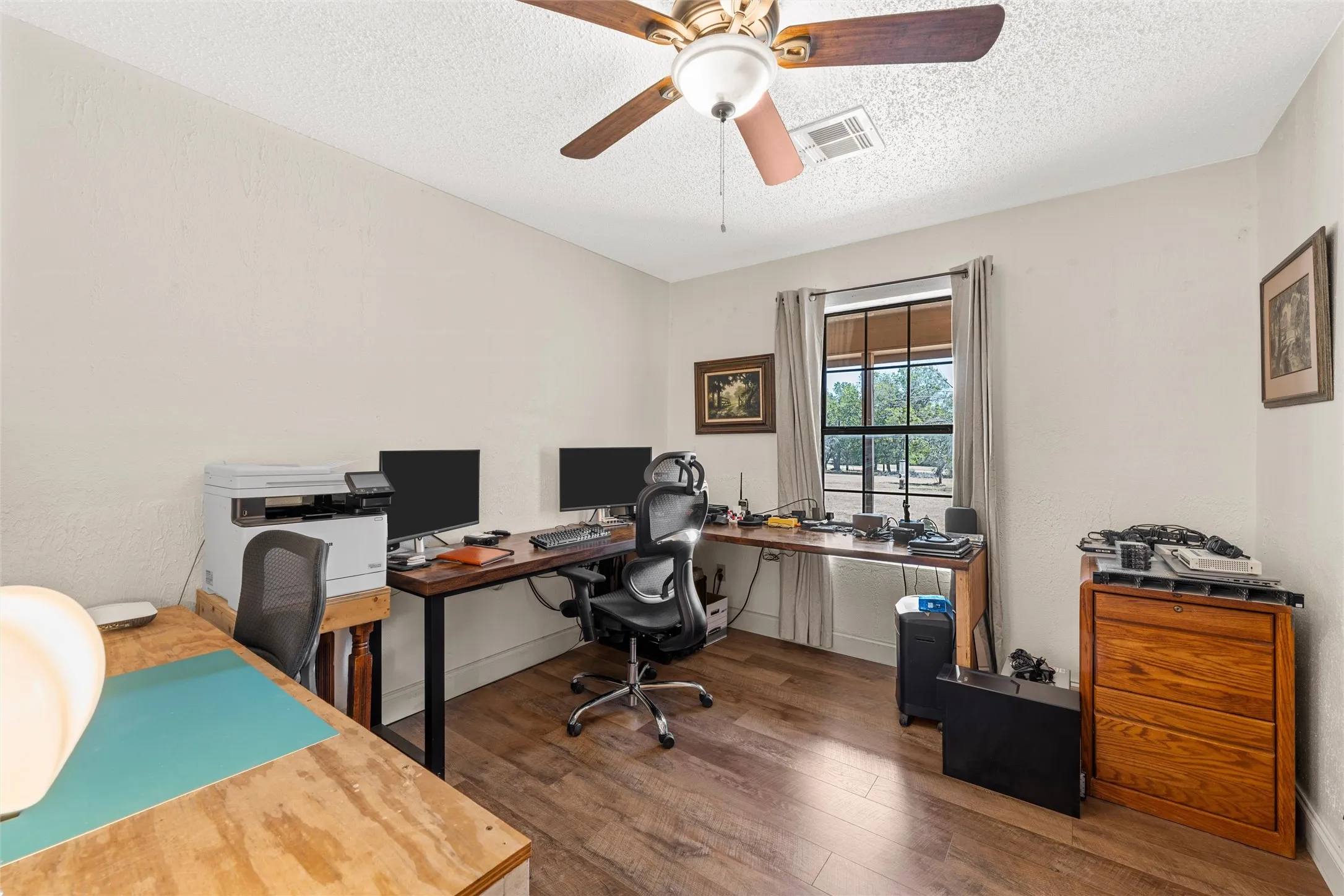 Wood-finish flooring, ceiling fan with light fixture, window with drapes, and textured walls