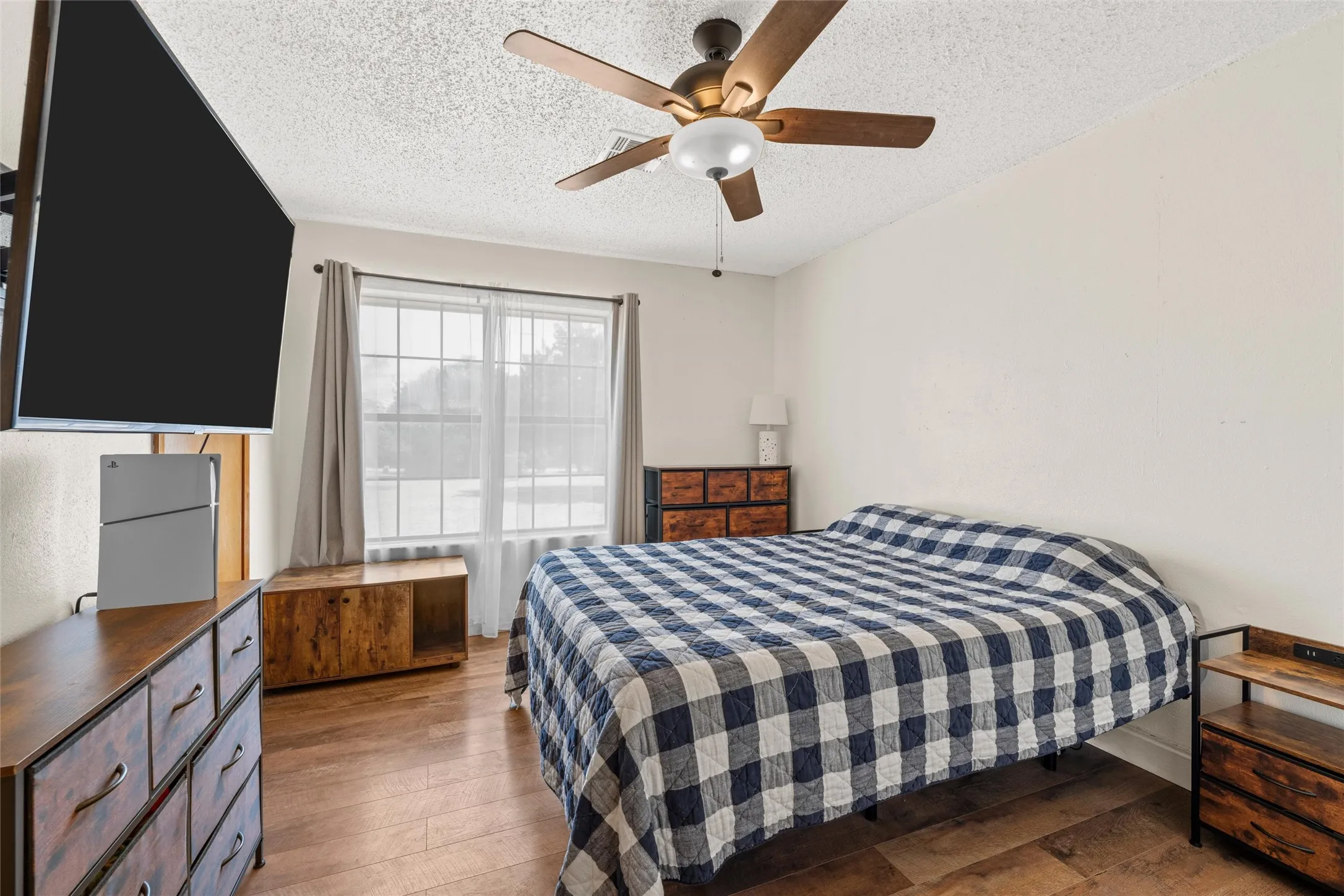 Wood-finish flooring, ceiling fan with integrated lighting, and window with light-filtering sheers