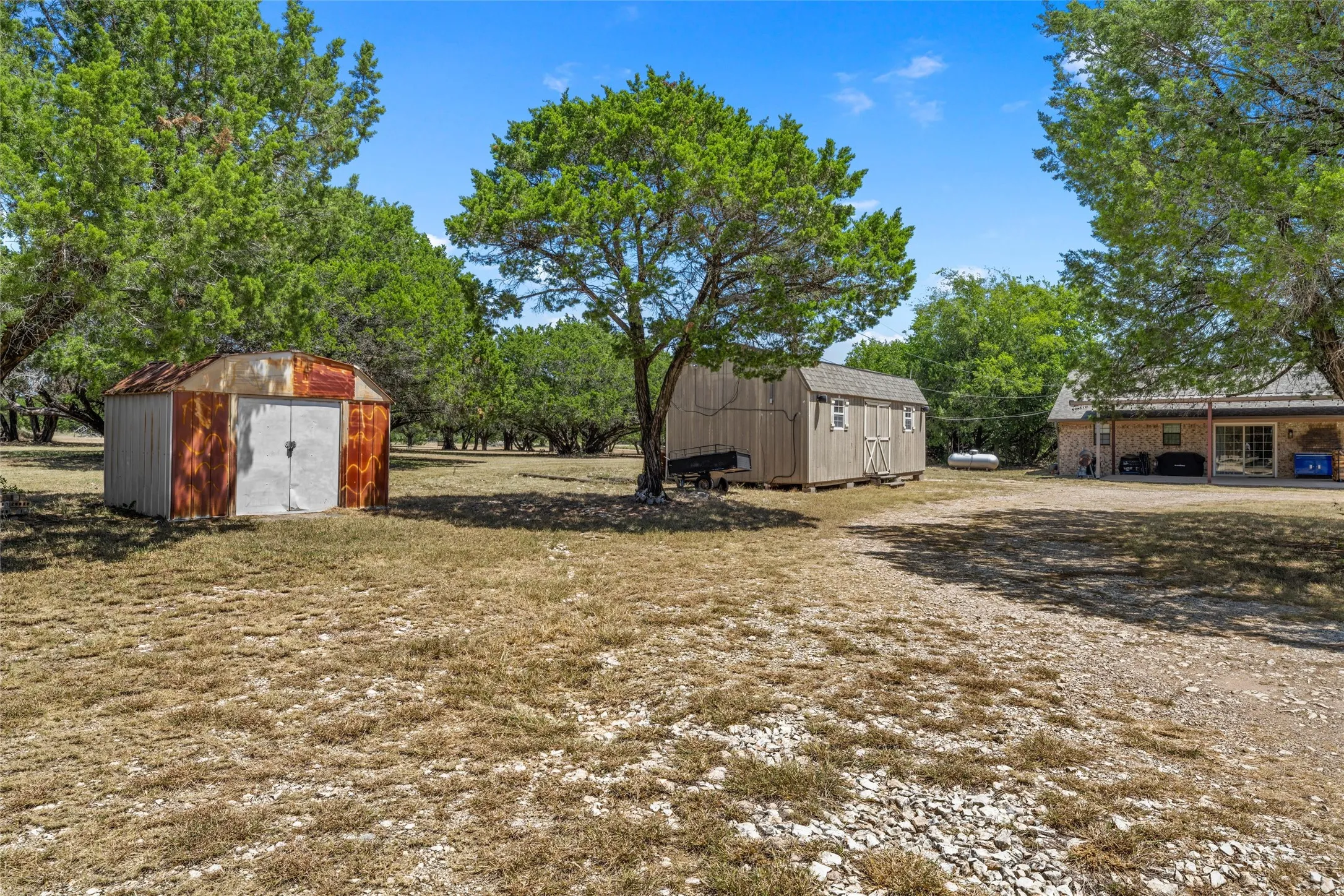 Expansive outdoor area featuring mature trees and a gravel driveway