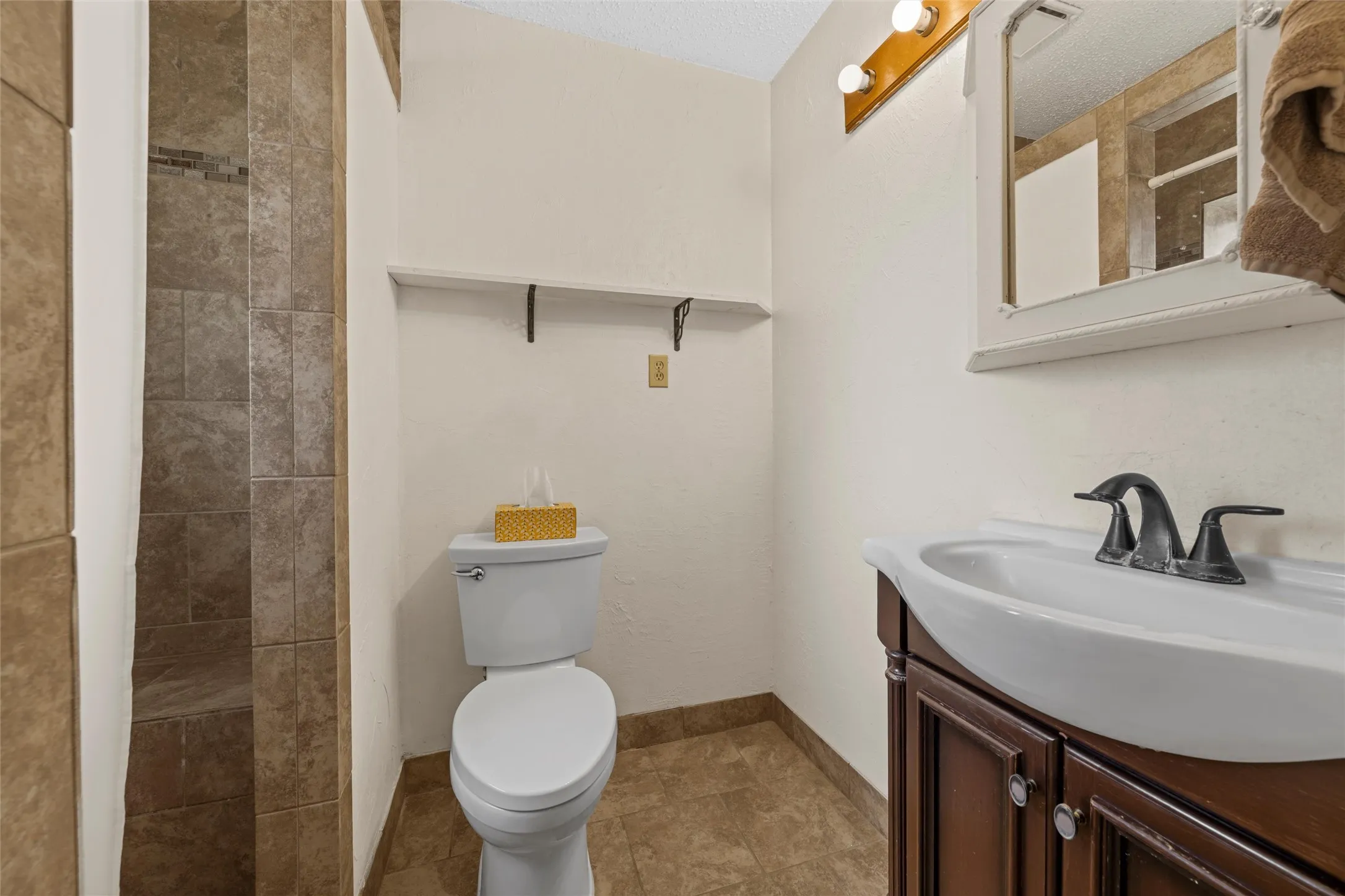 Tiled shower with a built-in bench, dark wood-finish vanity with a white basin, and a wall-mounted mirror