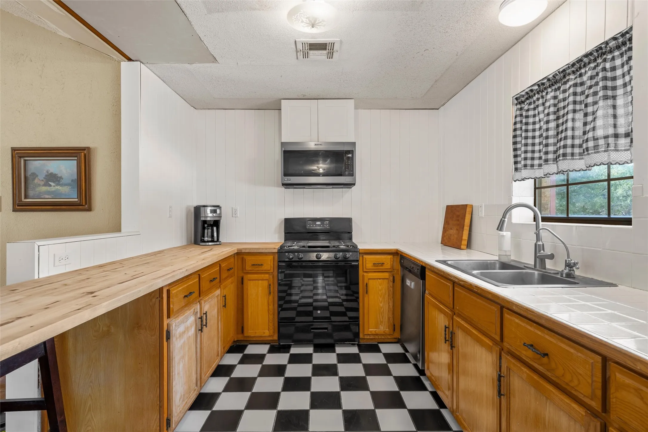 Kitchen featuring a checkered floor, wood-finish cabinetry, stainless steel sink, and white tile backsplash