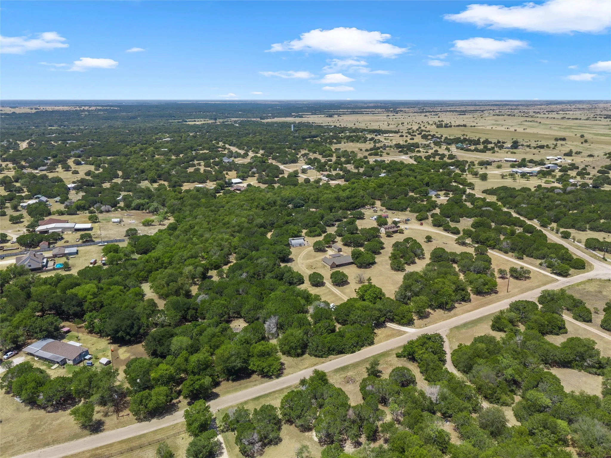 Expansive rural landscape featuring scattered residential structures, mature trees, and unpaved roads