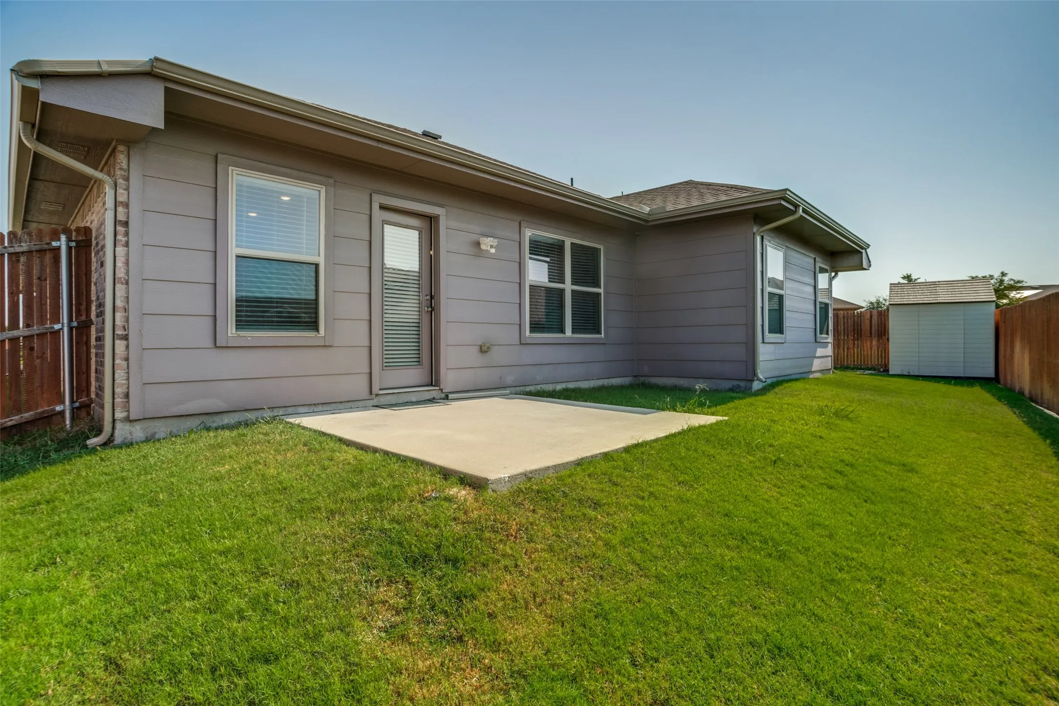 Expansive green space featuring a concrete patio, wood privacy fencing, and an exterior storage shed